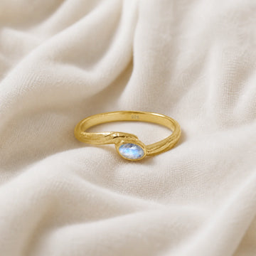 Cute_ring_gold_plated_silver_with_oval_moonstone_and_textured_wave_band_shown_at_front_angle_on_soft_fabric_background