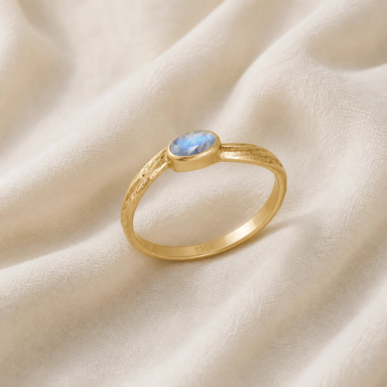 Cute_ring_gold_plated_silver_with_oval_moonstone_and_textured_wave_band_shown_slightly_tilted_on_soft_fabric_background