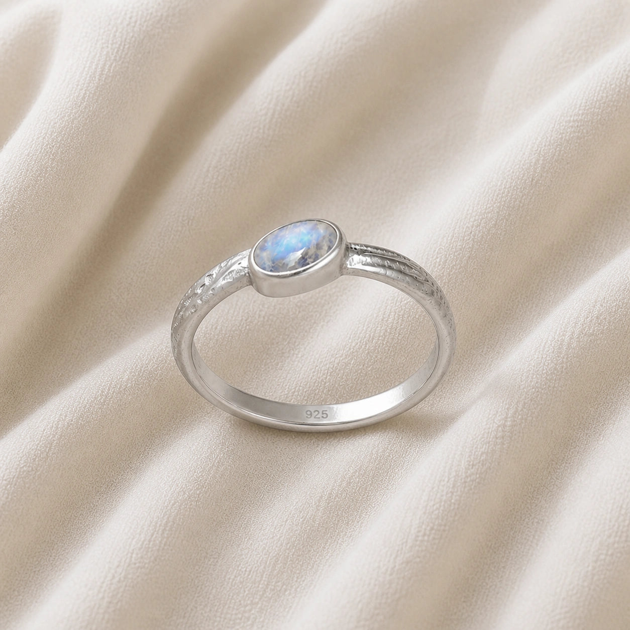 Cute_ring_sterling_silver_with_oval_moonstone_and_textured_wave_band_shown_slightly_tilted_on_soft_fabric_background