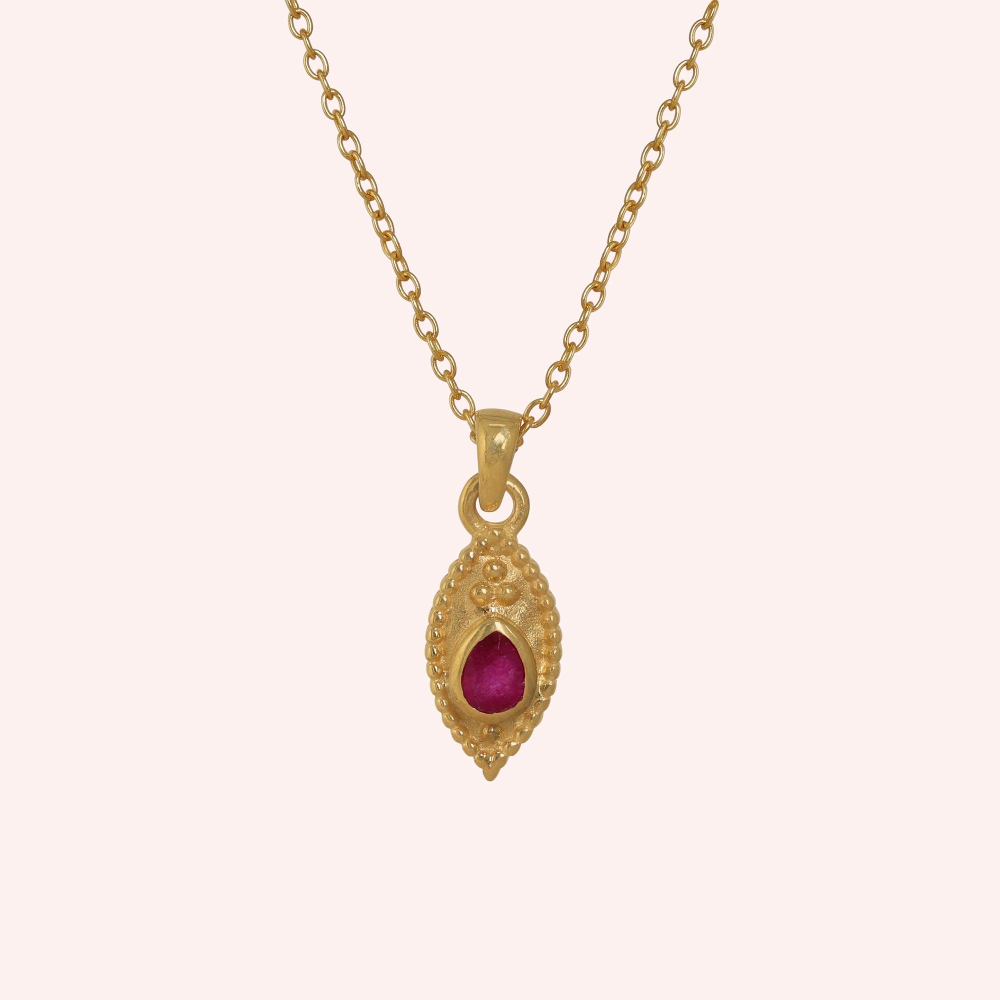Dainty_necklace_in_gold_plated_silver_front_angle_with_ruby_teardrop_pendant_on_solid_pink_background