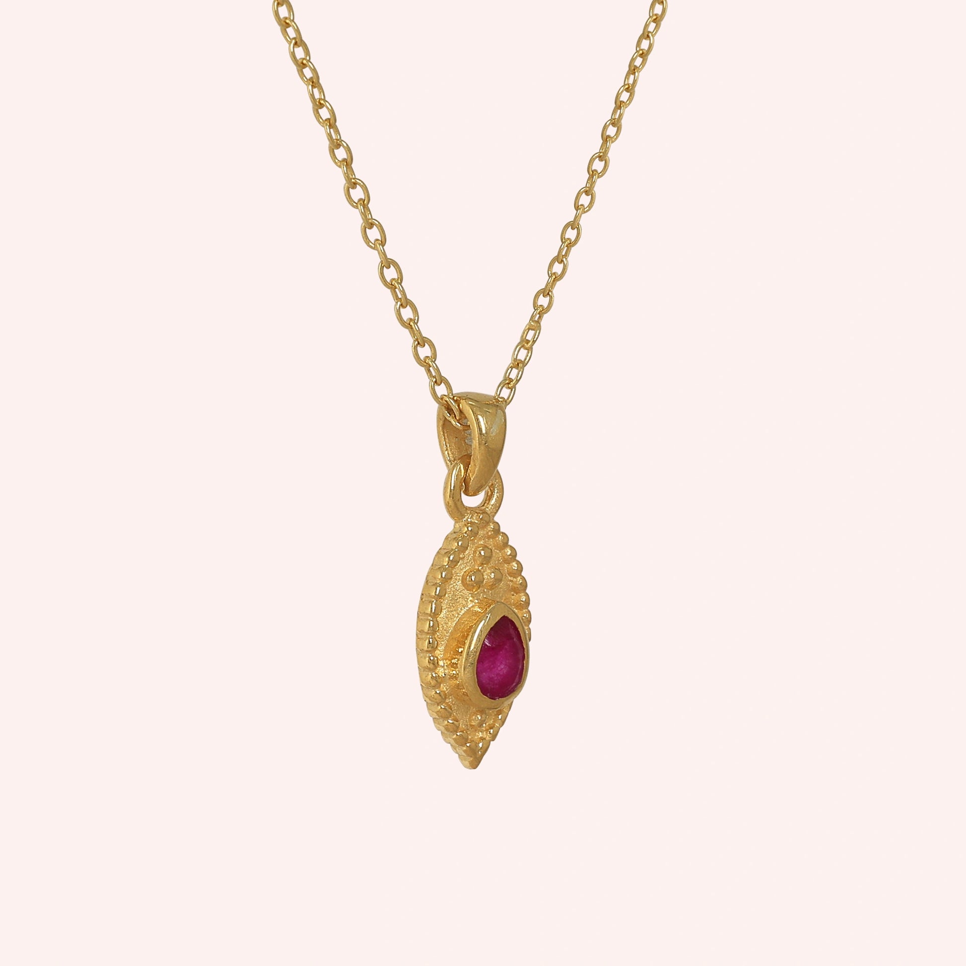 Dainty_necklace_in_gold_plated_silver_slightly_angled_with_ruby_teardrop_pendant_on_solid_pink_background