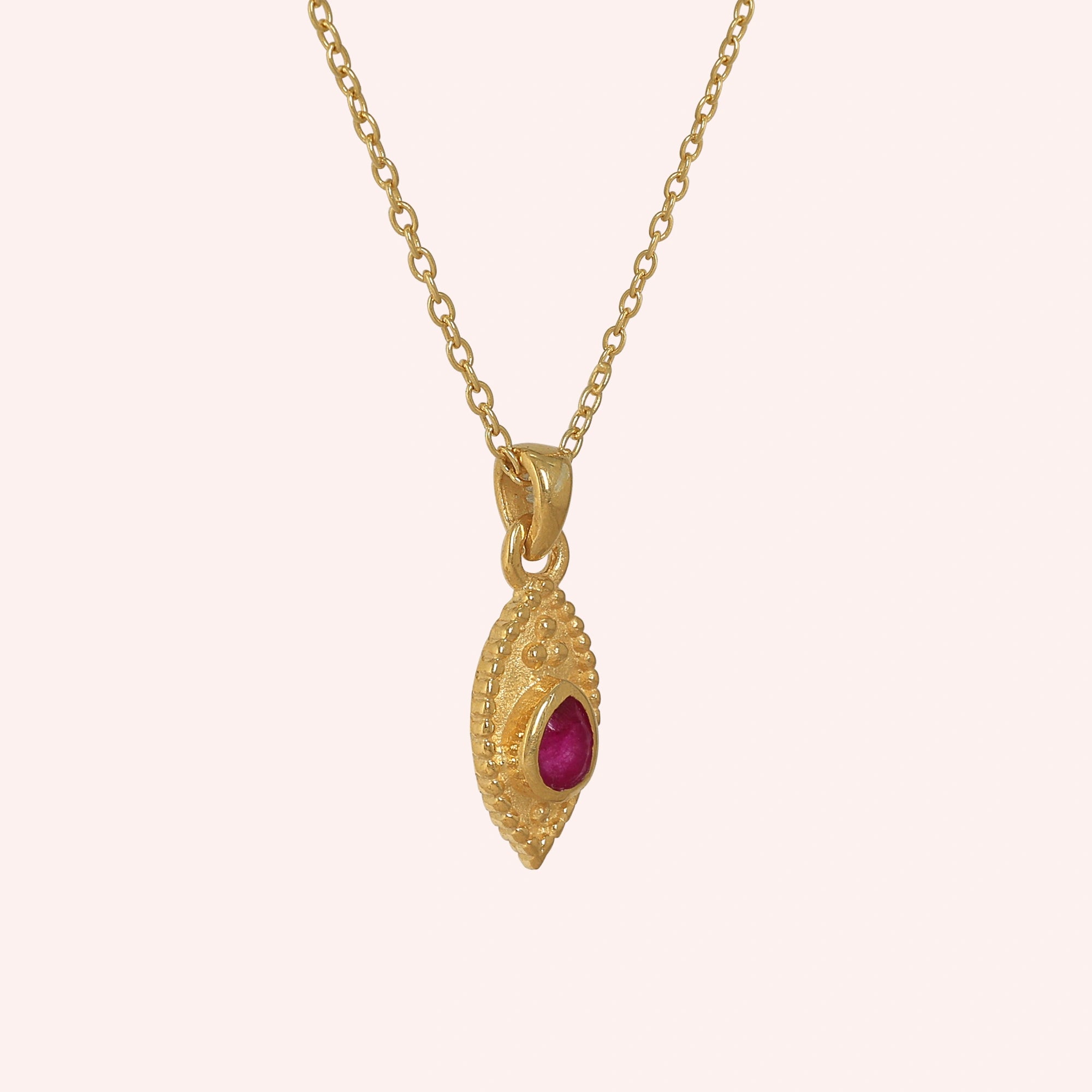 Dainty_necklace_in_gold_plated_silver_slightly_angled_with_ruby_teardrop_pendant_on_solid_pink_background