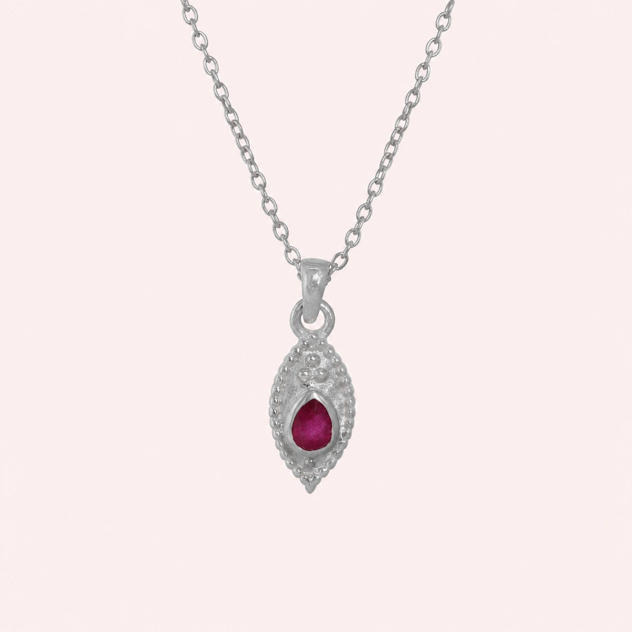 Dainty_necklace_in_sterling_silver_front_angle_with_ruby_teardrop_pendant_on_solid_pink_background