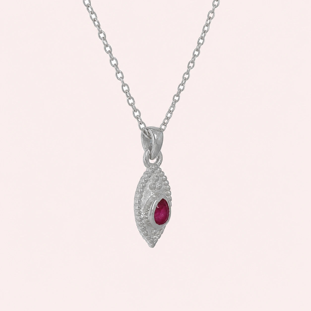 Dainty_necklace_in_sterling_silver_slightly_angled_with_ruby_teardrop_pendant_on_solid_pink_background