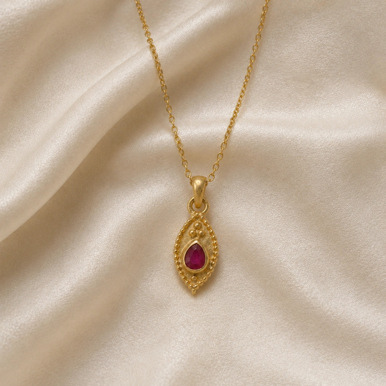 Dainty_necklace_in_gold_plated_silver_front_angle_with_ruby_teardrop_pendant_on_soft_fabric_background