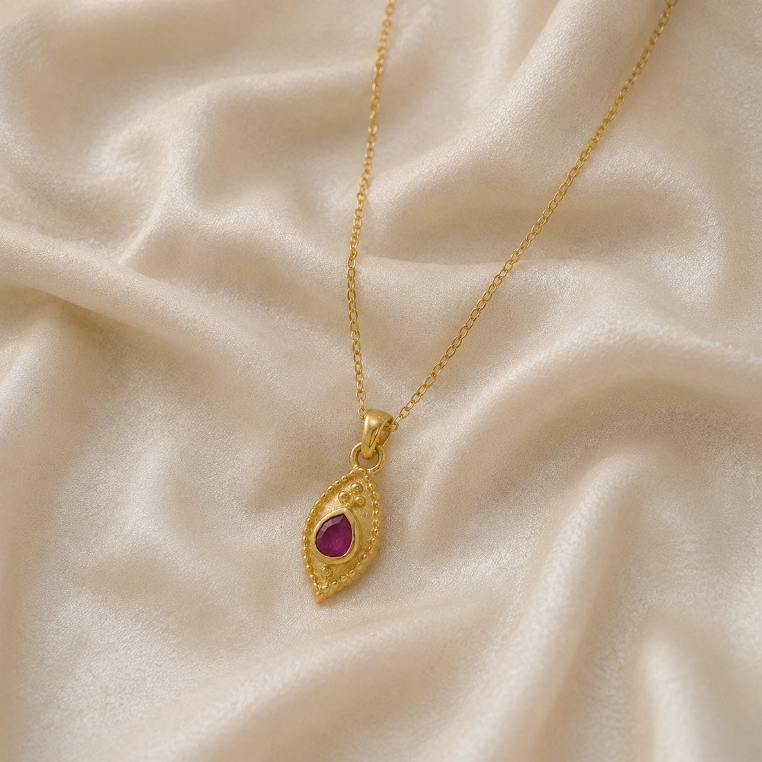 Dainty_necklace_in_gold_plated_silver_slightly_angled_with_ruby_teardrop_pendant_on_soft_fabric_background