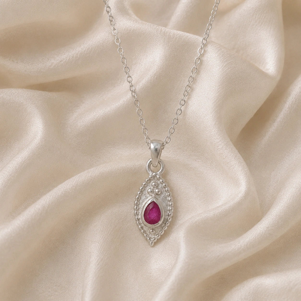 Dainty_necklace_in_sterling_silver_front_angle_with_ruby_teardrop_pendant_on_soft_fabric_background