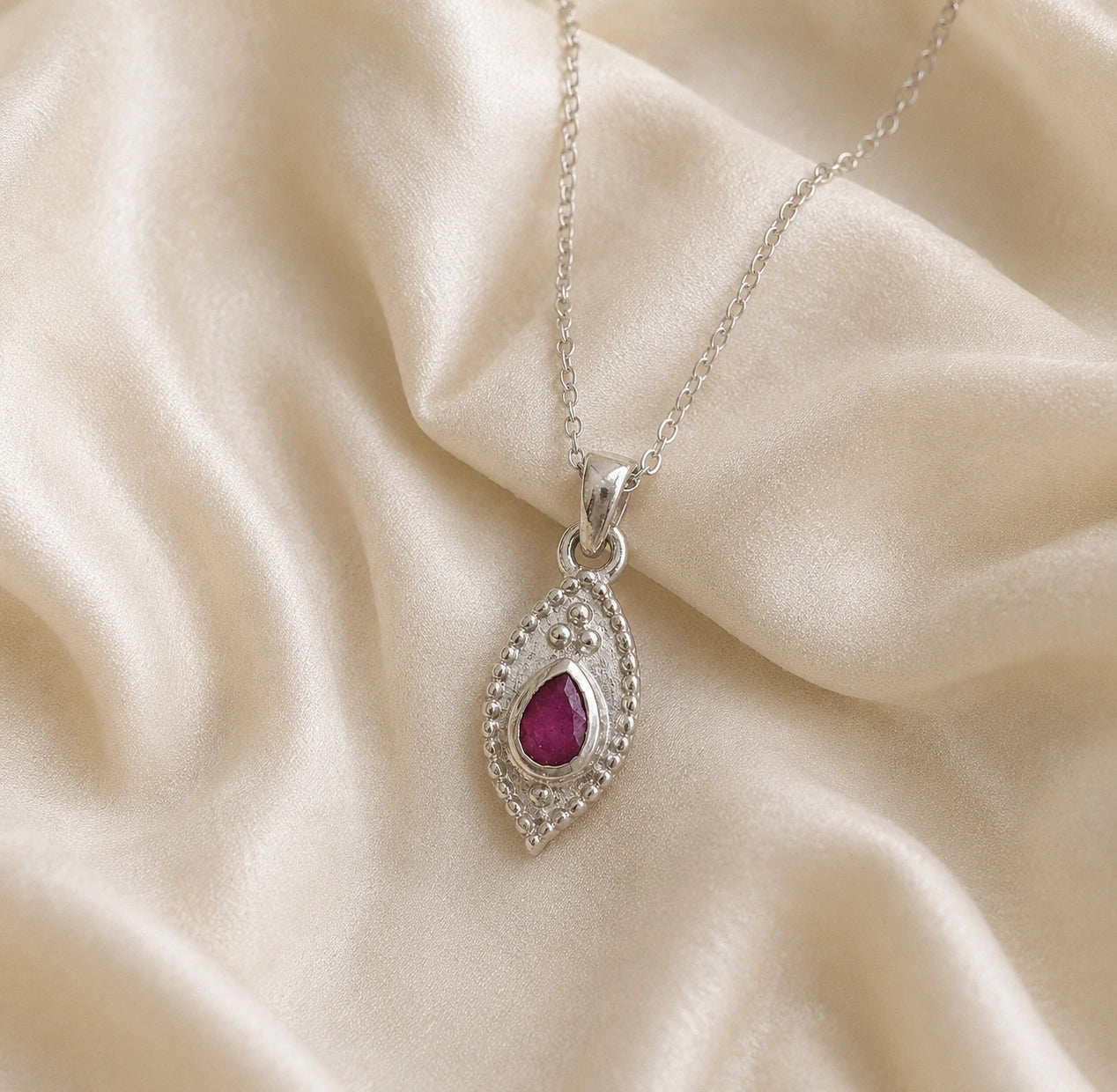 Dainty_necklace_in_sterling_silver_slightly_angled_with_ruby_teardrop_pendant_on_soft_fabric_background