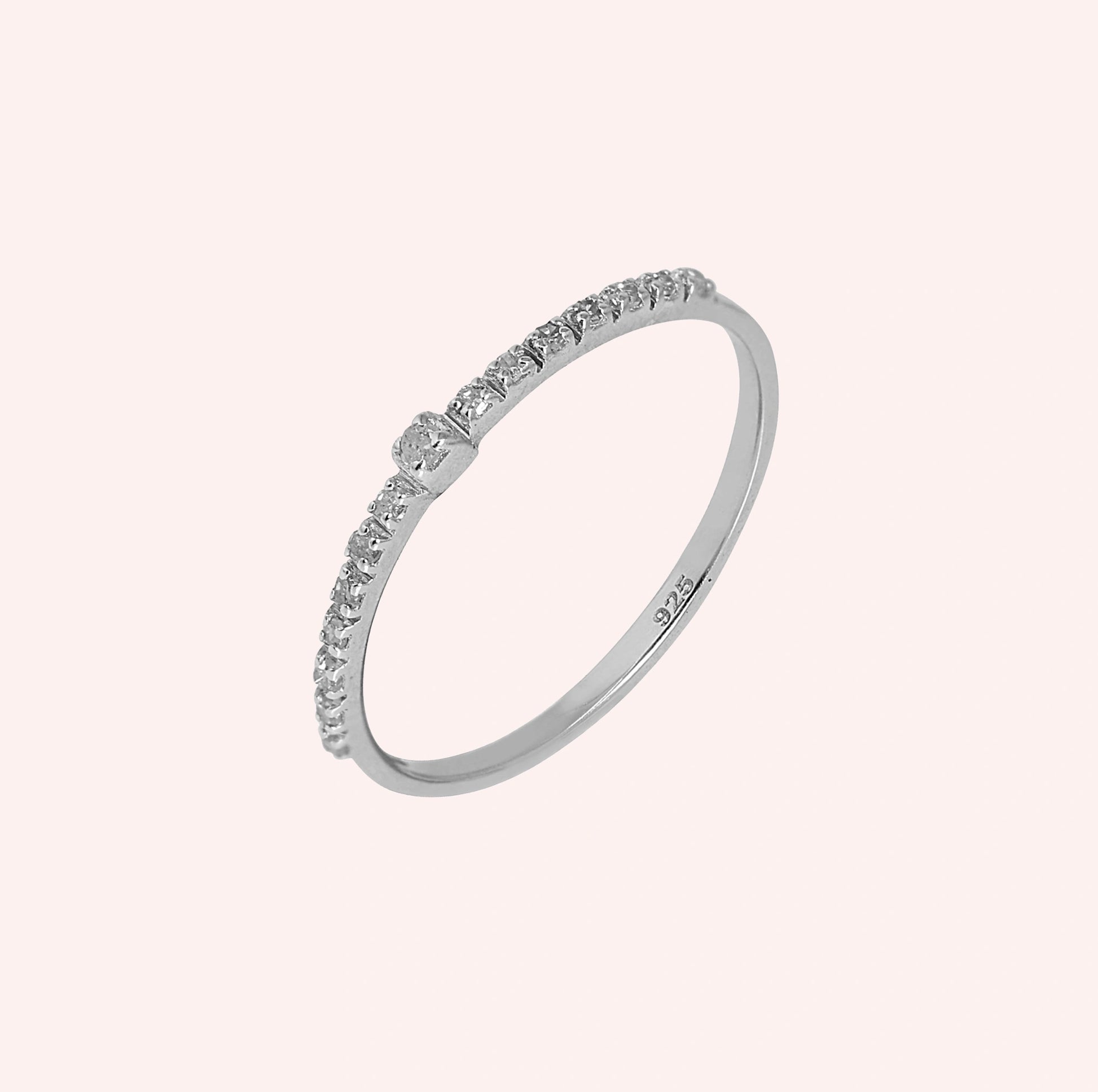 Dainty_ring_in_sterling_silver_at_front_angle_featuring_diamonds_on_solid_pink_background