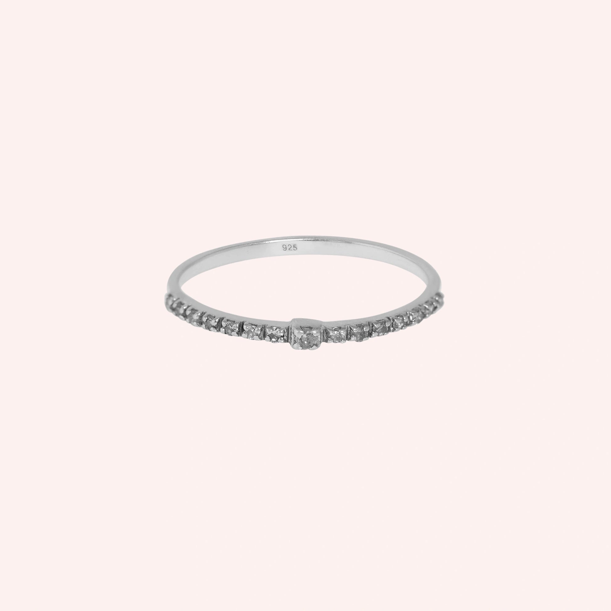 Dainty_ring_in_sterling_silver_at_front_angle_featuring_diamonds_on_solid_pink_background
