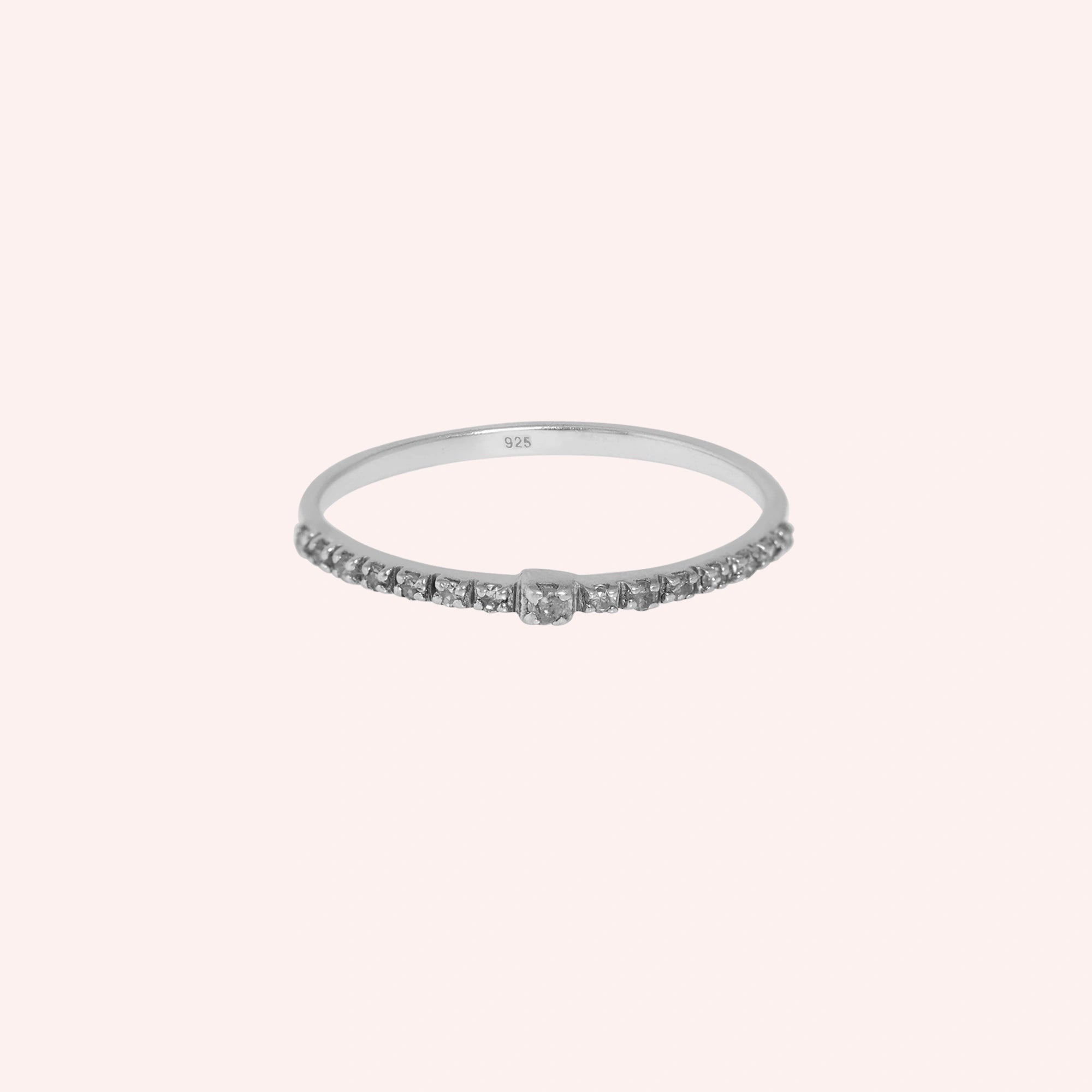 Dainty_ring_in_sterling_silver_at_front_angle_featuring_diamonds_on_solid_pink_background