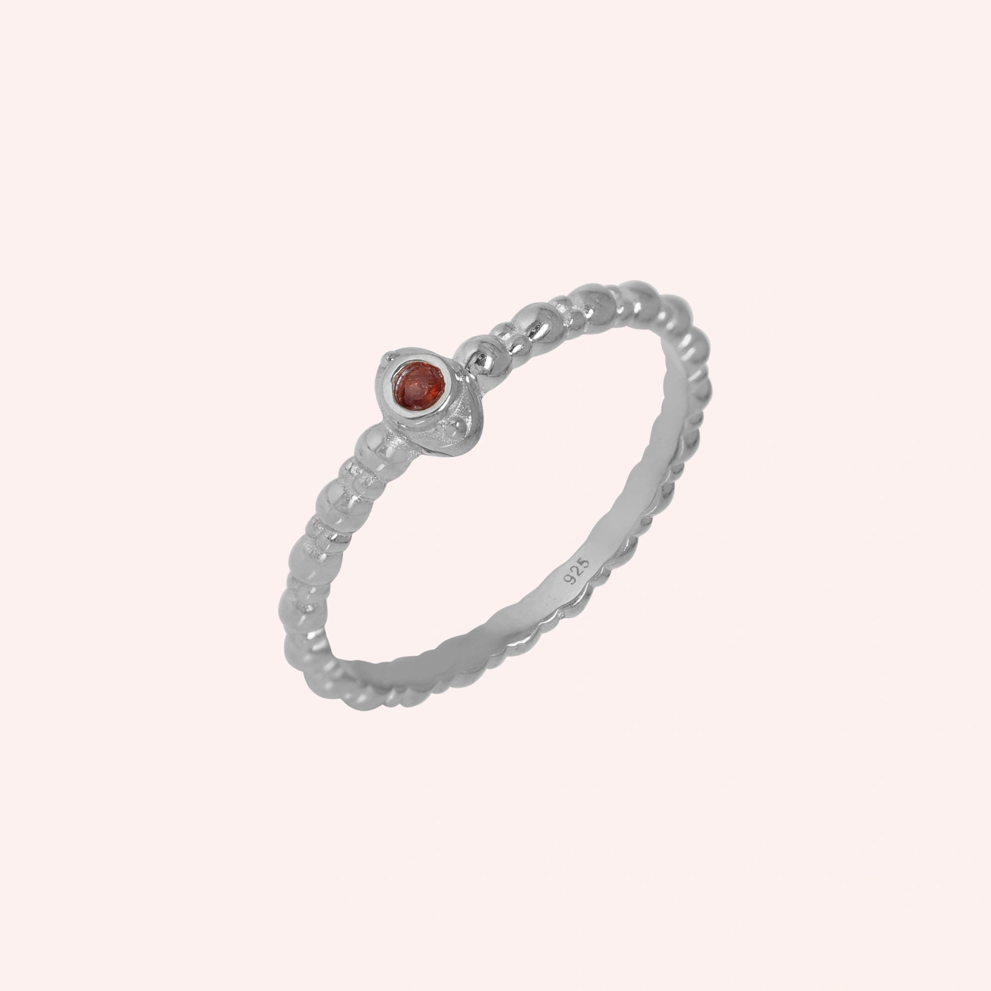 Dainty-ring-with-red-garnet-gemstone-sterling-silver-angled-view-on-soft-pink-background