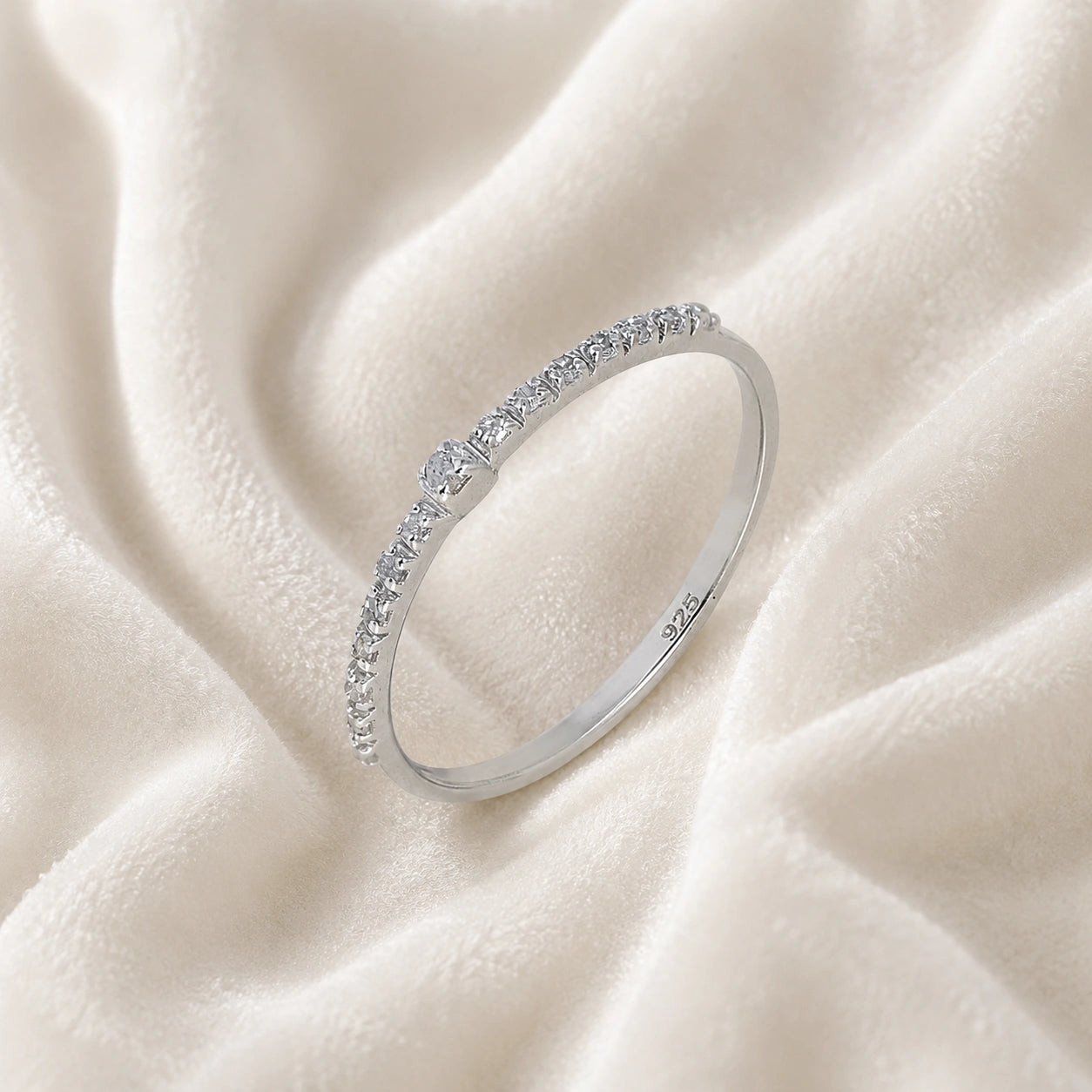 Dainty_ring_in_sterling_silver_at_slight_angle_featuring_diamonds_on_soft_fabric_background