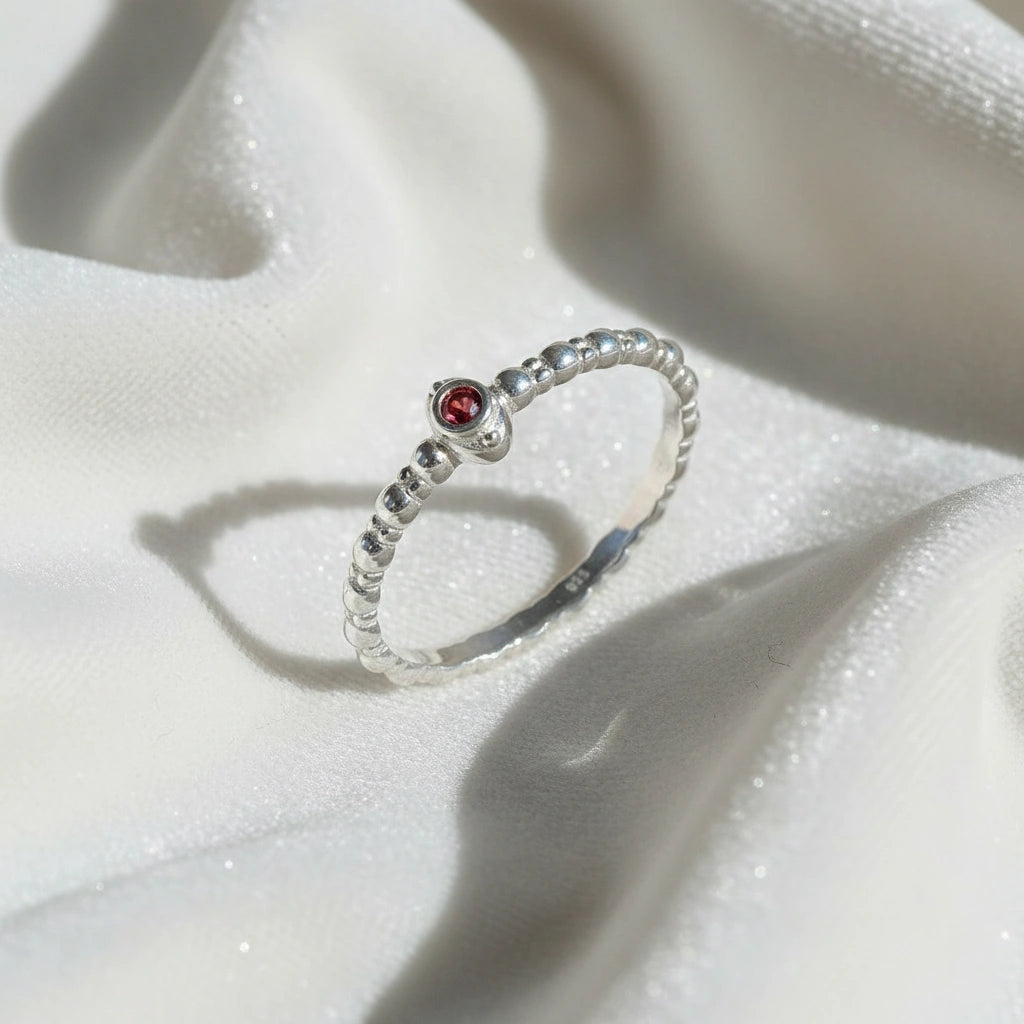 Dainty-ring-with-red-garnet-gemstone-sterling-silver-angled-view-on-white-satin-background