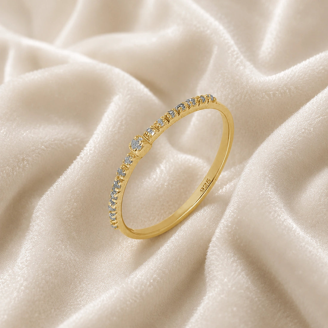 Dainty_ring_in_gold_plated_silver_at_slight_angle_featuring_diamonds_on_soft_fabric_background