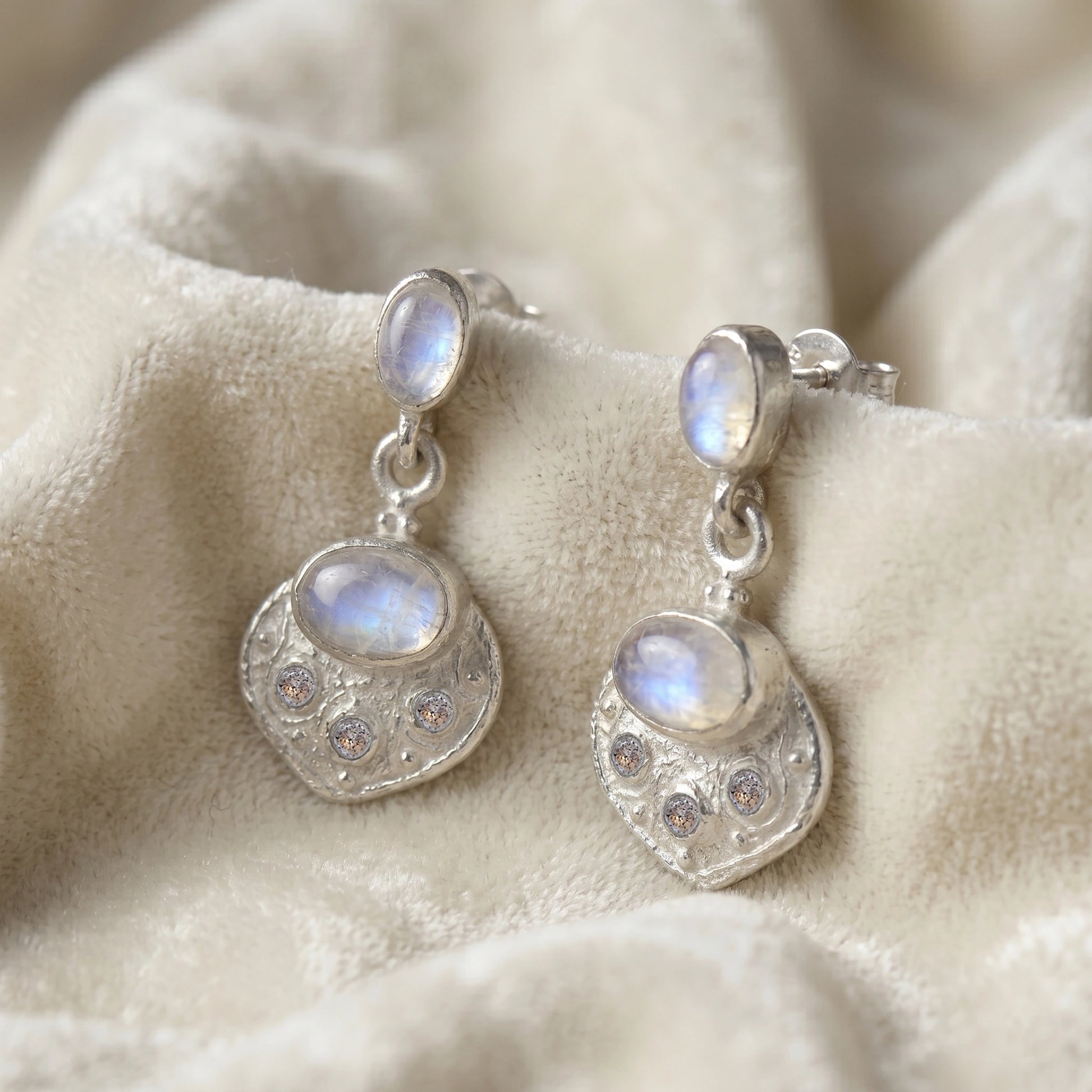 Dangle_earrings_in_sterling_silver_with_moonstone_and_labradorite_shown_at_slightly_angled_on_soft_velvet_fabric_background