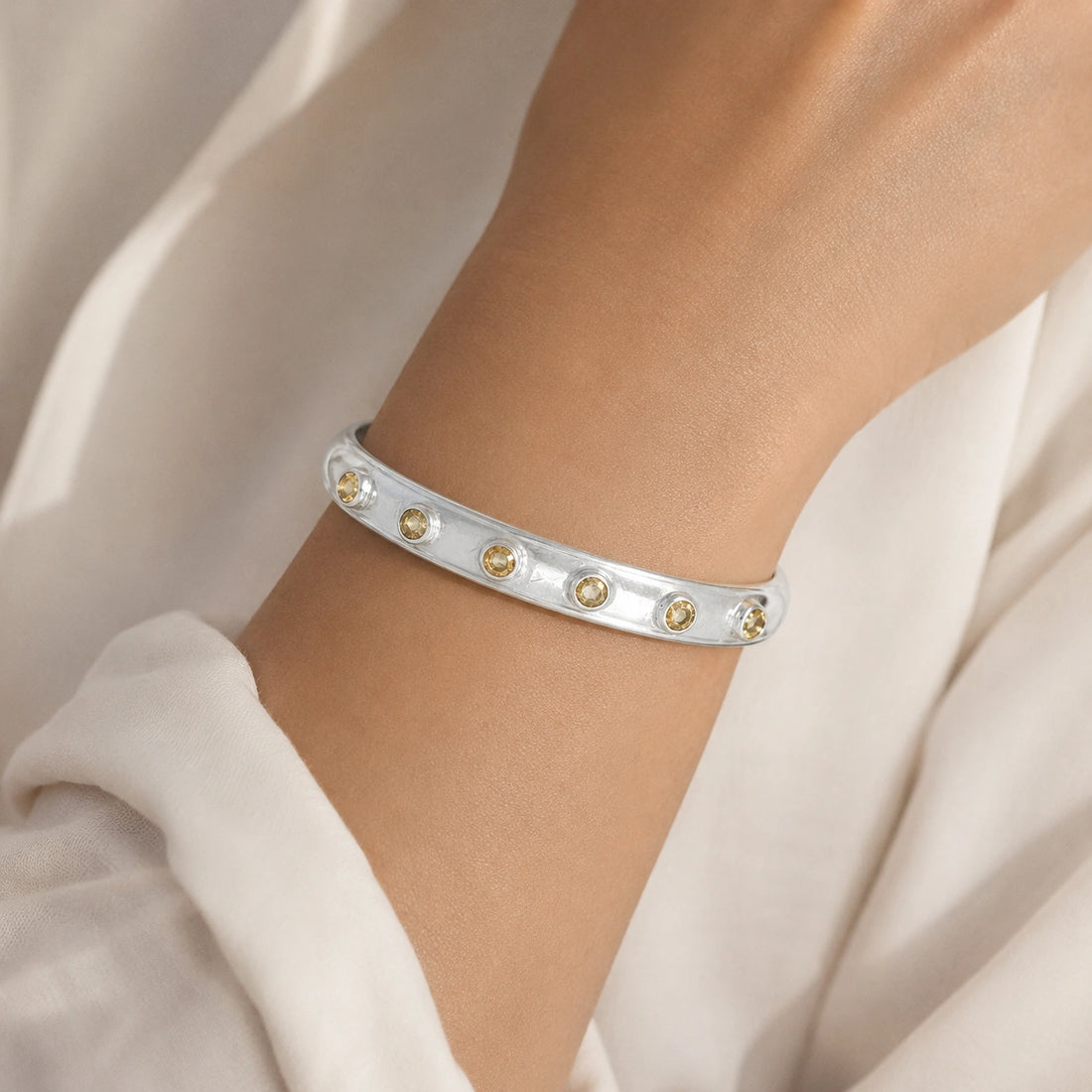 Designer_bangle_in_gold_plated_silver_with_bezel_set_citrine_stones_at_slight_view_on_soft_fabric_background