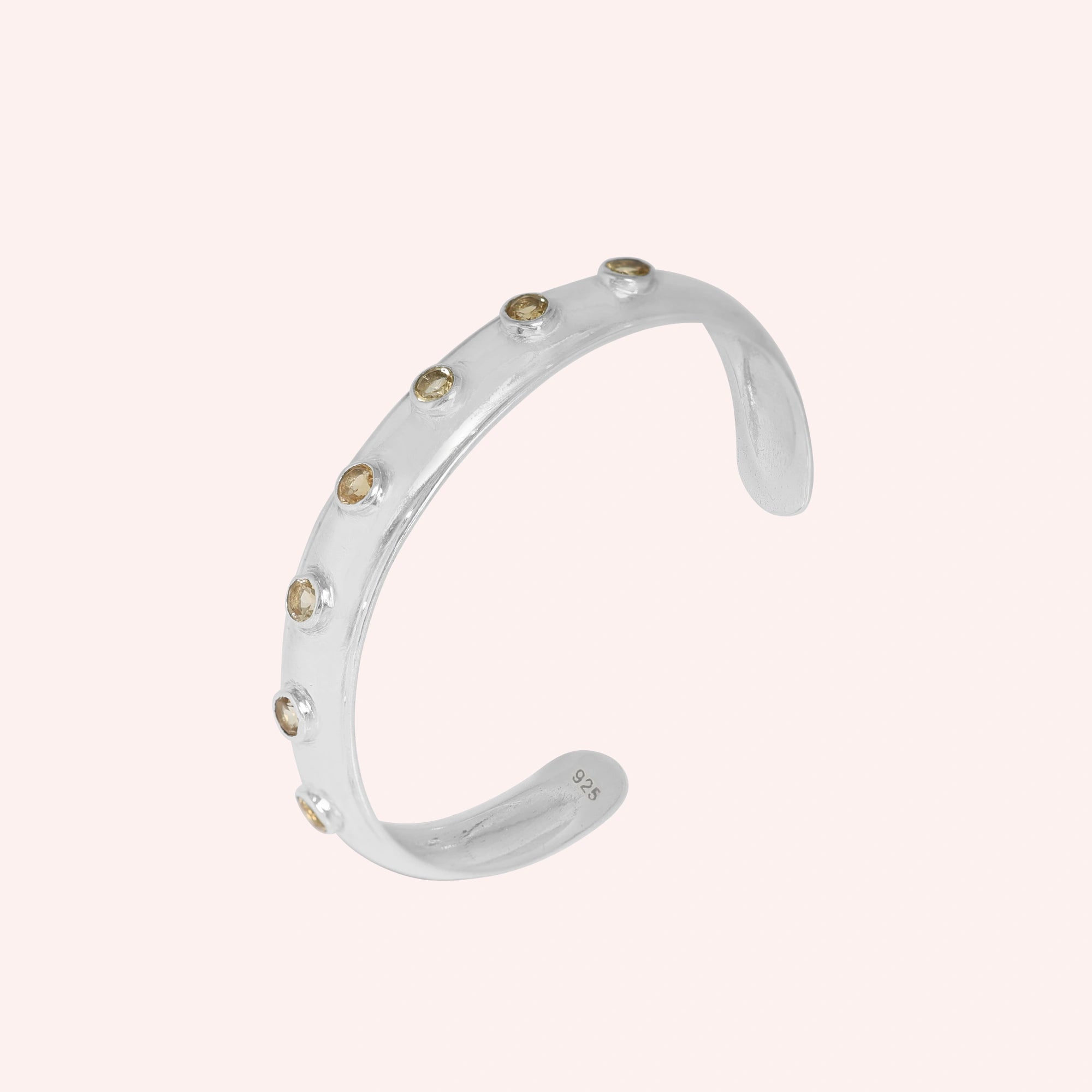 Designer_bangle_in_sterling_silver_with_bezel_set_citrine_stones_at_slight_view_on_solid_pink_background