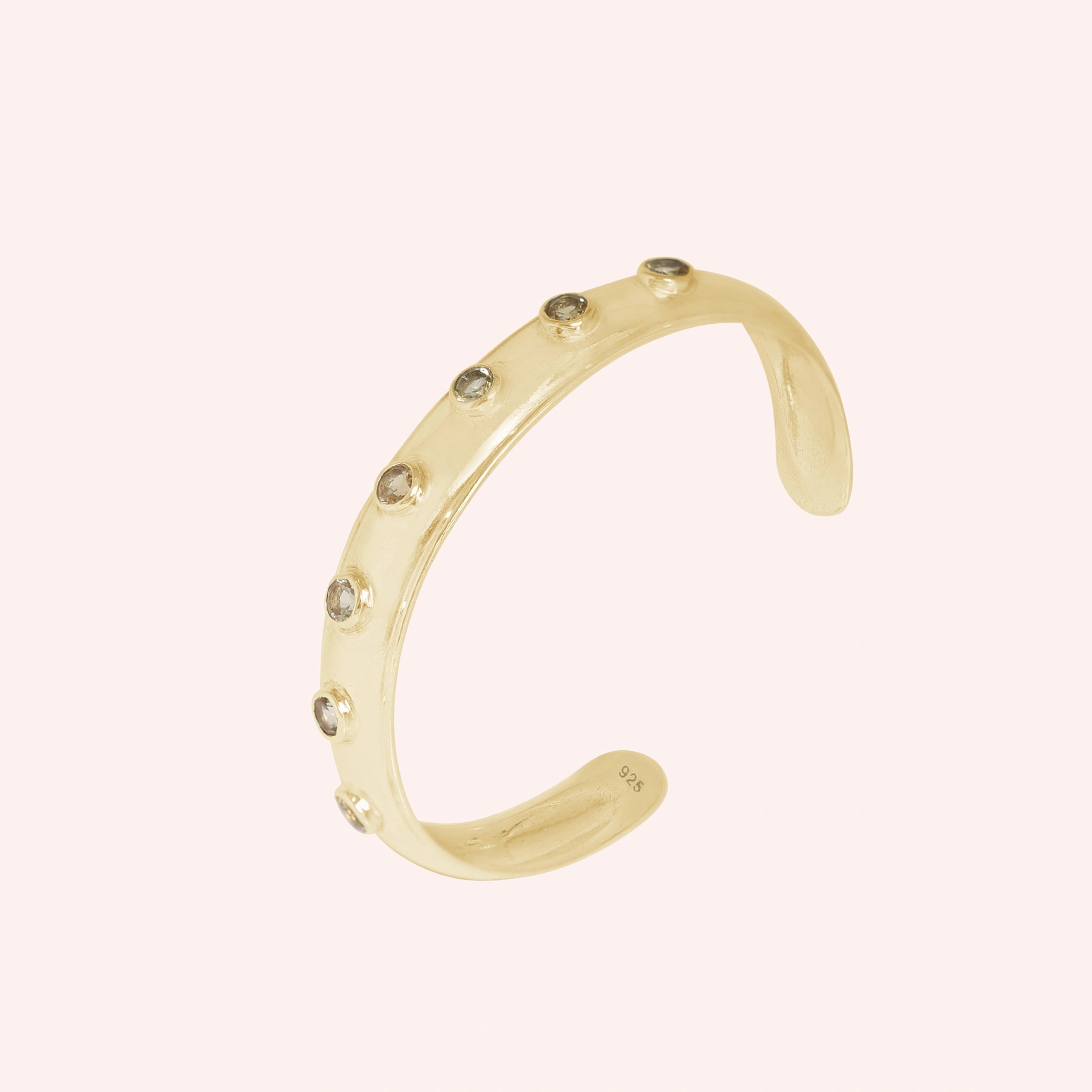 Designer_bangle_in_gold_plated_silver_with_bezel_set_citrine_stones_at_slight_view_on_solid_pink_background