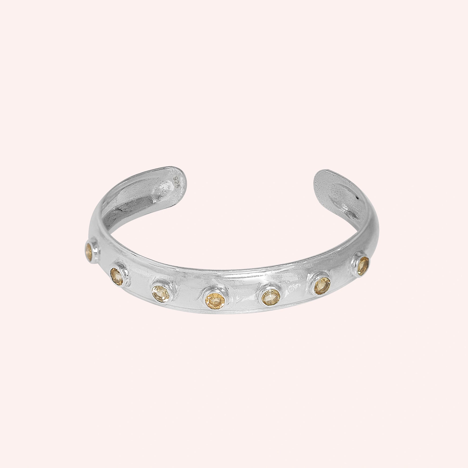 Designer_bangle_in_sterling_silver_with_bezel_set_citrine_stones_at_front_view_on_solid_pink_background