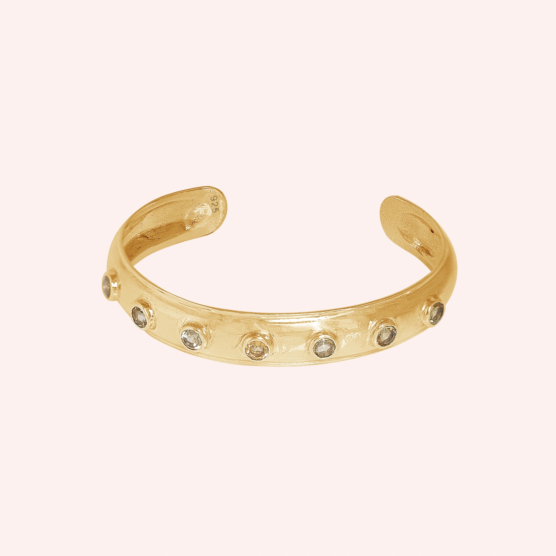 Designer_bangle_in_gold_plated_silver_with_bezel_set_citrine_stones_at_front_view_on_solid_pink_background