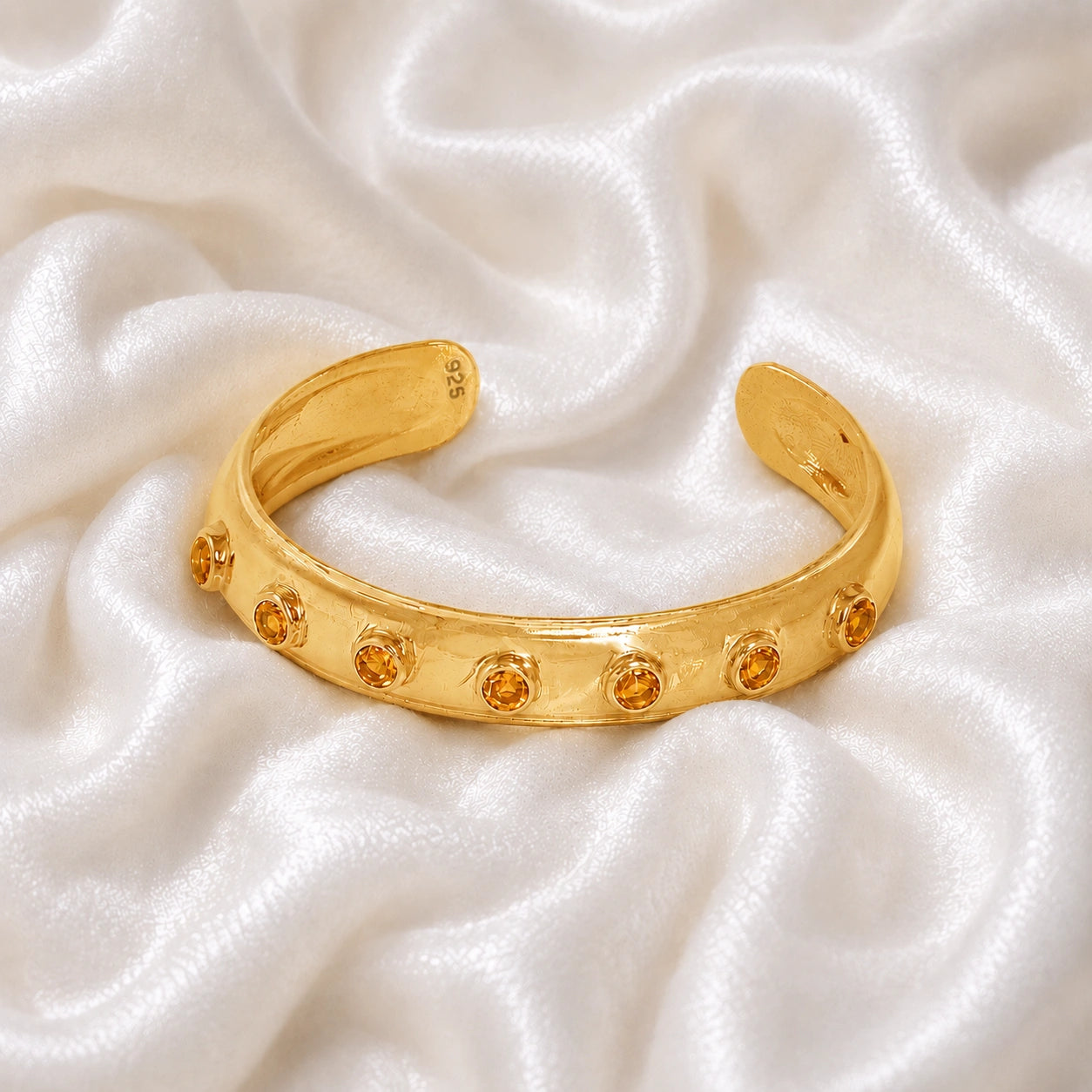 Designer_bangle_in_gold_plated_silver_with_bezel_set_citrine_stones_at_front_view_on_soft_fabric_background