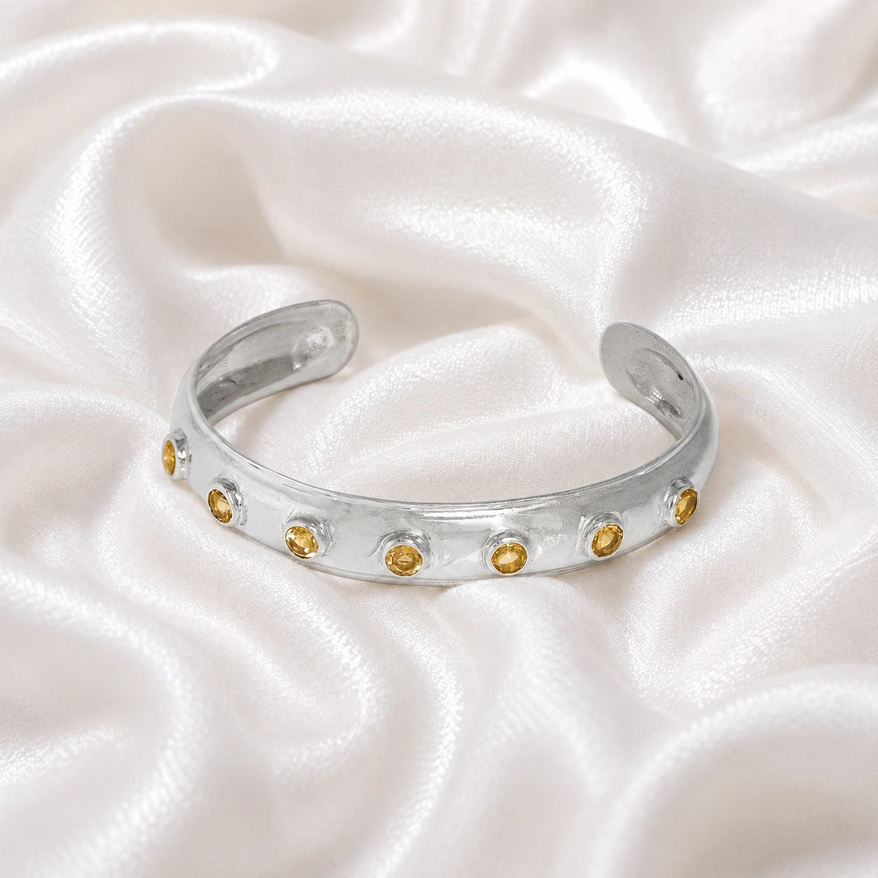 Designer_bangle_in_sterling_silver_with_bezel_set_citrine_stones_at_front_view_on_soft_fabric_background