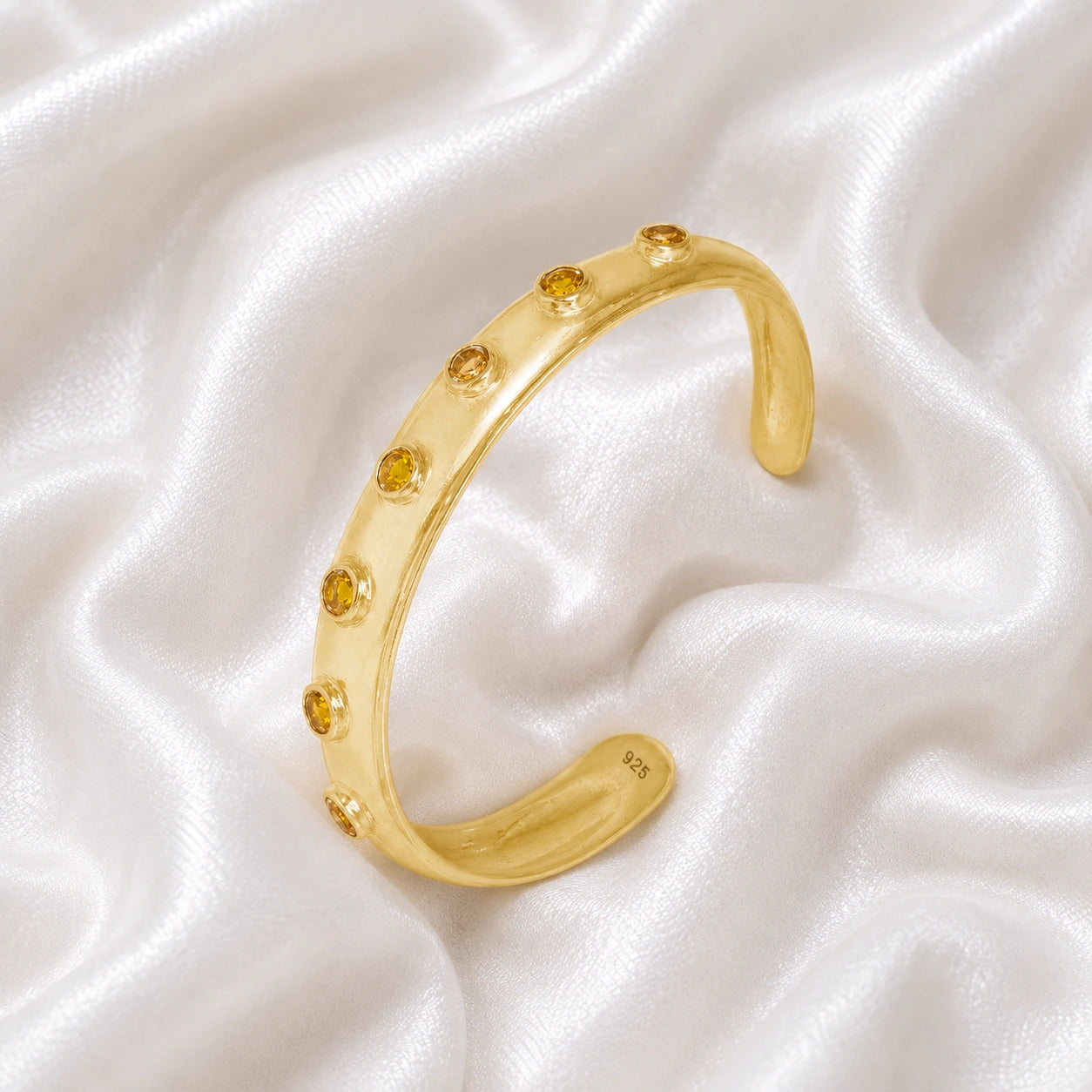 Designer_bangle_in_gold_plated_silver_with_bezel_set_citrine_stones_at_slight_view_on_soft_fabric_background