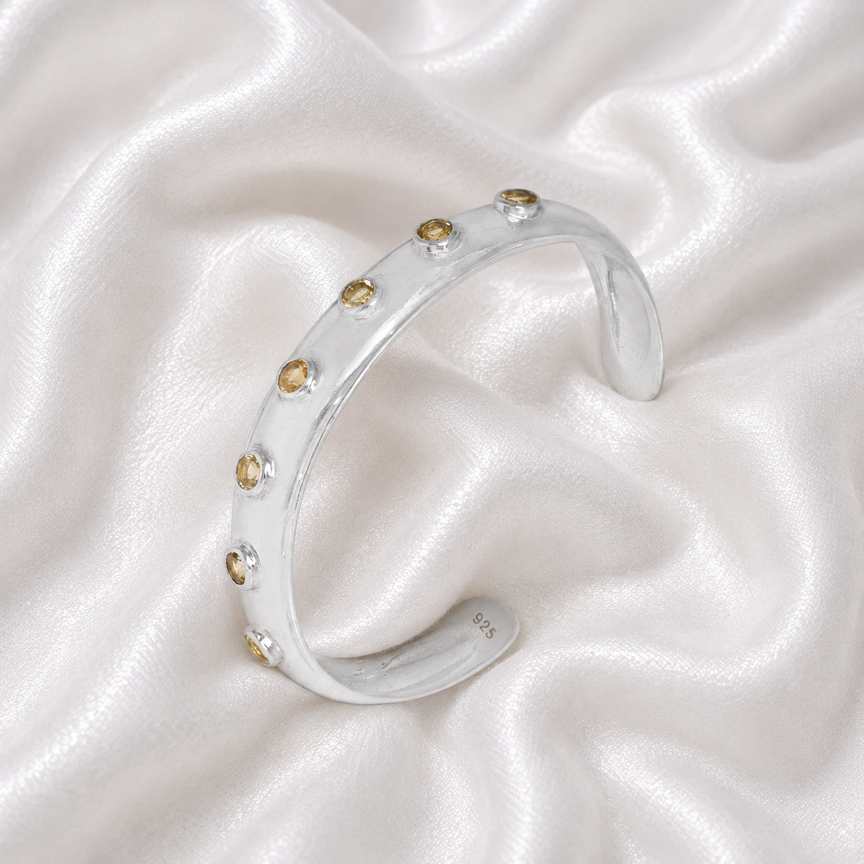 Designer_bangle_in_sterling_silver_with_bezel_set_citrine_stones_at_slight_view_on_soft_fabric_background