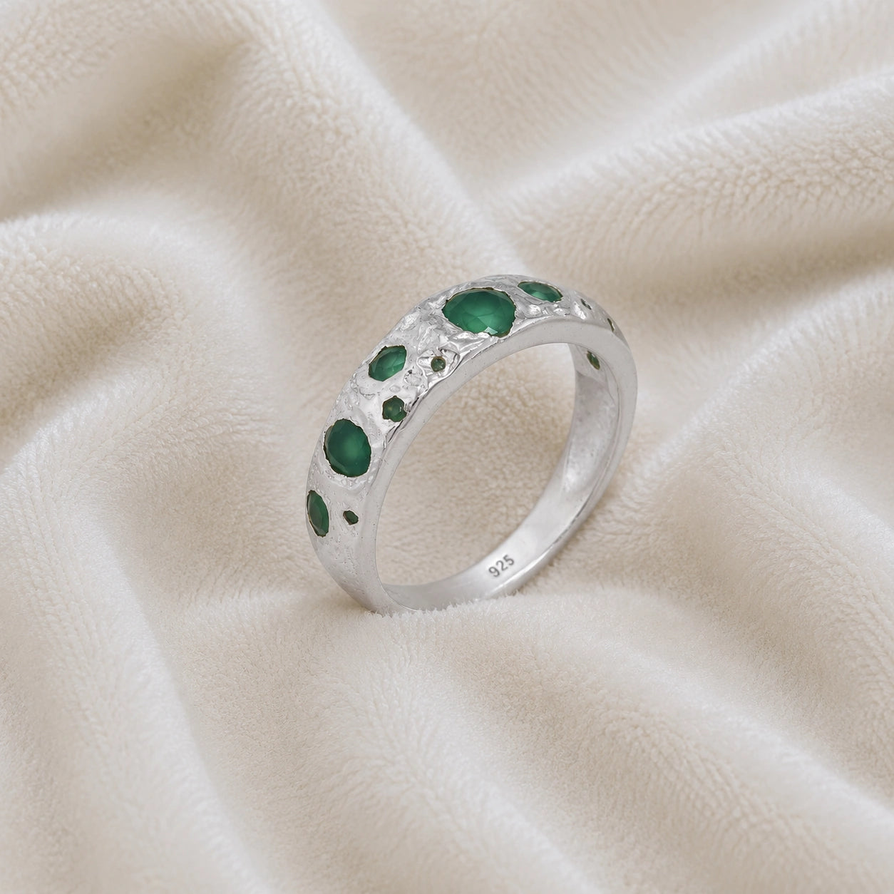 Designer_ring_in_sterling_silver_with_multiple_green_onyx_stones_at_slight_angle_on_soft_fabric_background