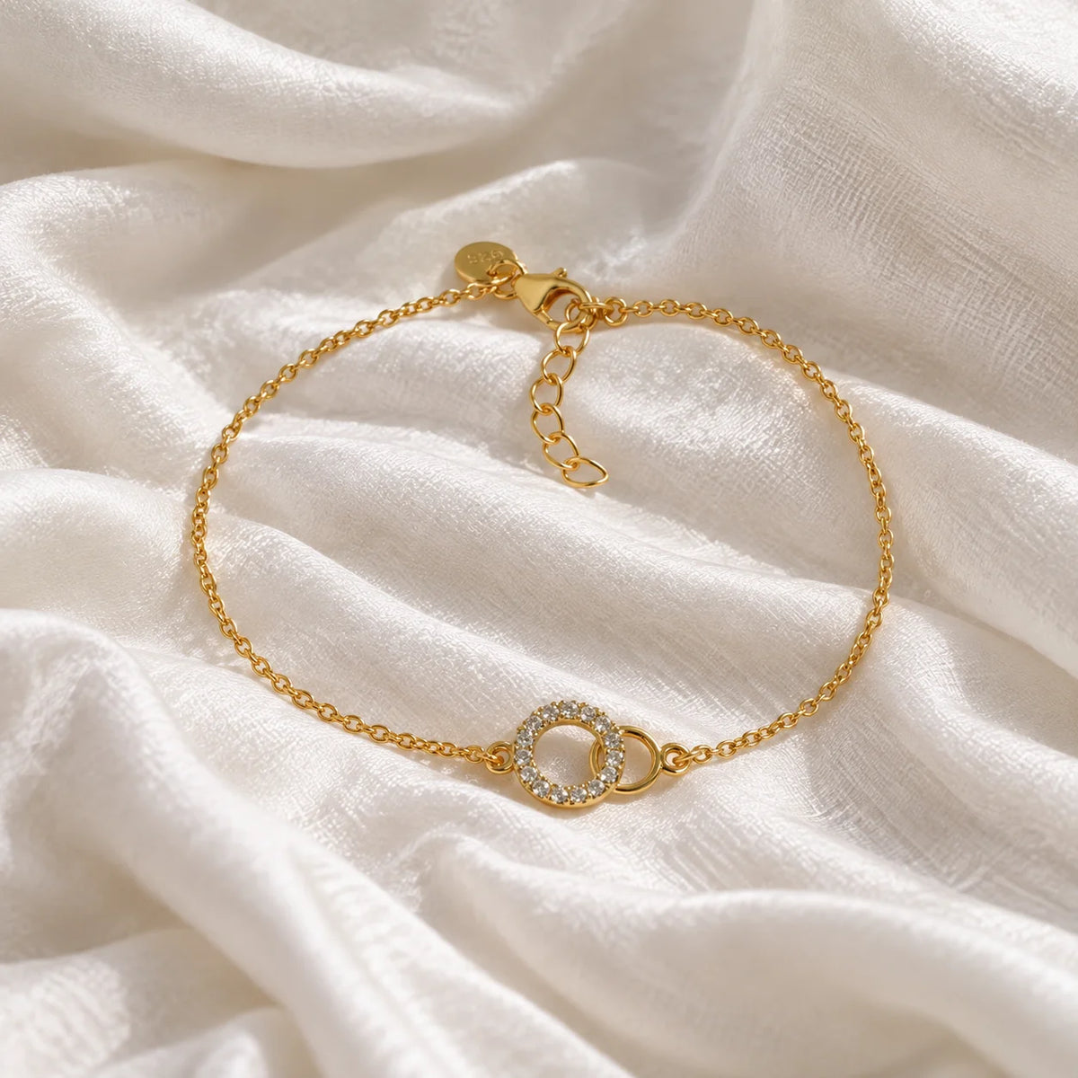 Diamond_bracelet_in_gold_plated_silver_in_an_interlocking_design_at_front_angle_view_on_soft_fabric_background