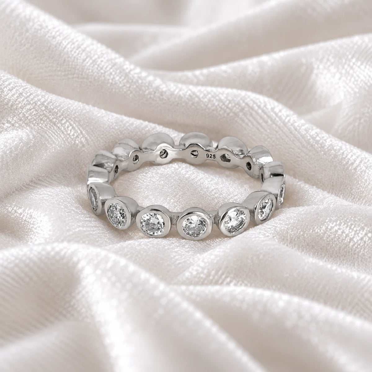 Diamond_eternity_ring_in_sterling_silver_with_lab_grown_diamonds_at_front_angle_view_on_soft_fabric_background