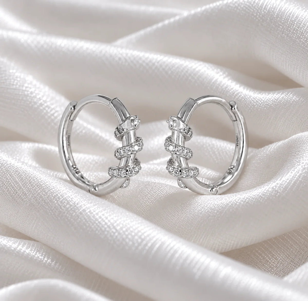 Diamond_hoop_earrings_in_sterling_silver_with_a_twisted_design_band_at_front_angle_view_on_soft_fabric_background