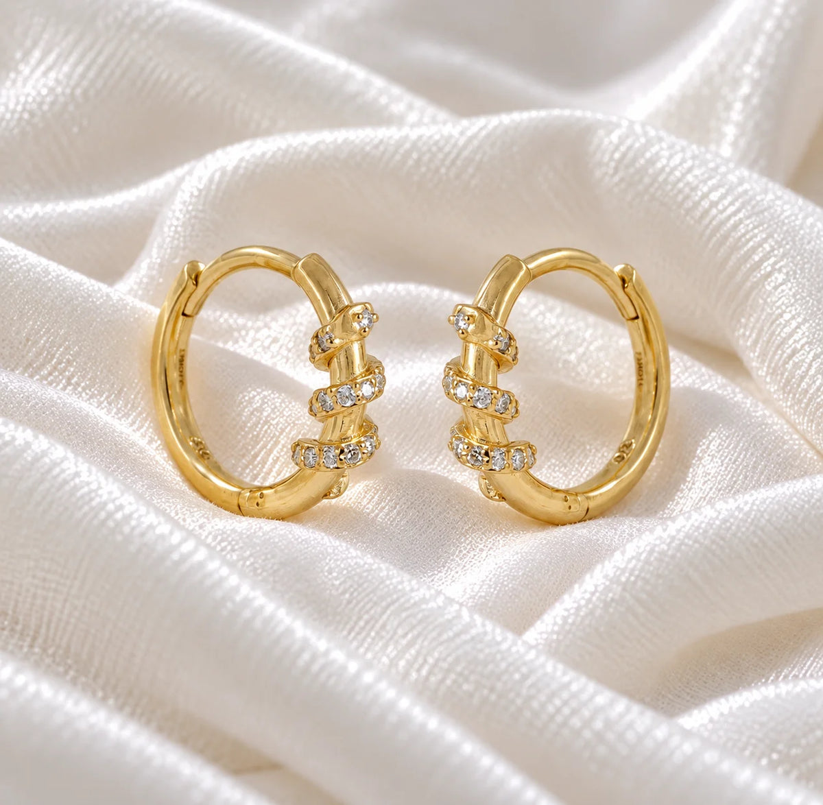 Diamond_hoop_earrings_in_gold_plated_silver_with_a_twisted_design_band_at_side_angle_view_on_soft_fabric_background