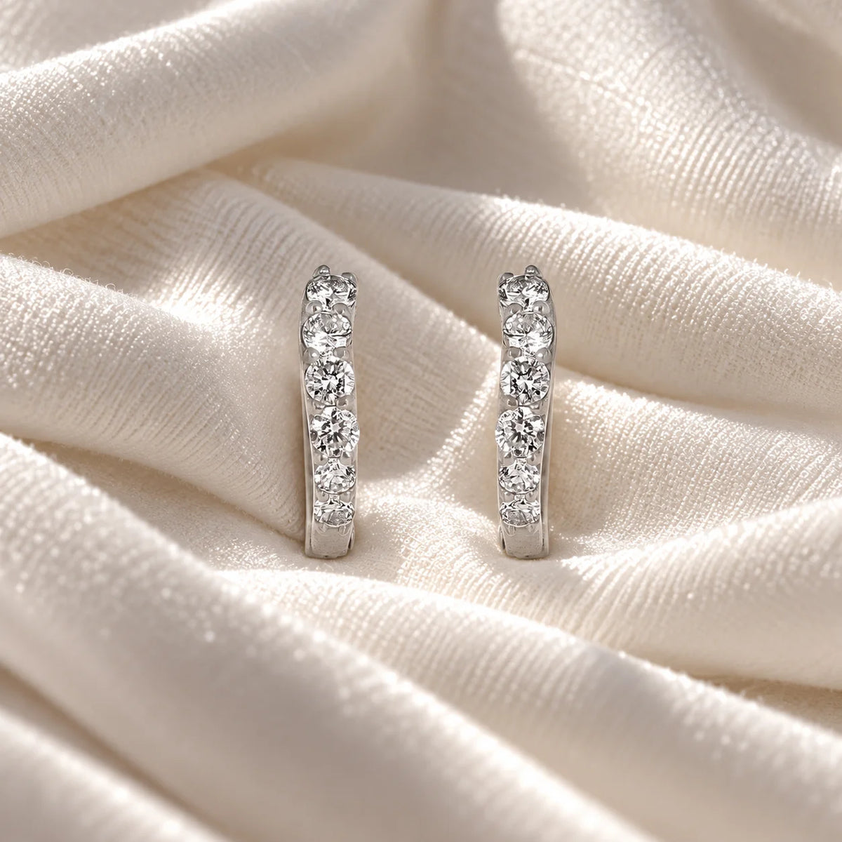 Diamond_hoop_earrings_in_sterling_silver_with_lab_grown_diamonds_at_front_angle_view_on_soft_fabric_background