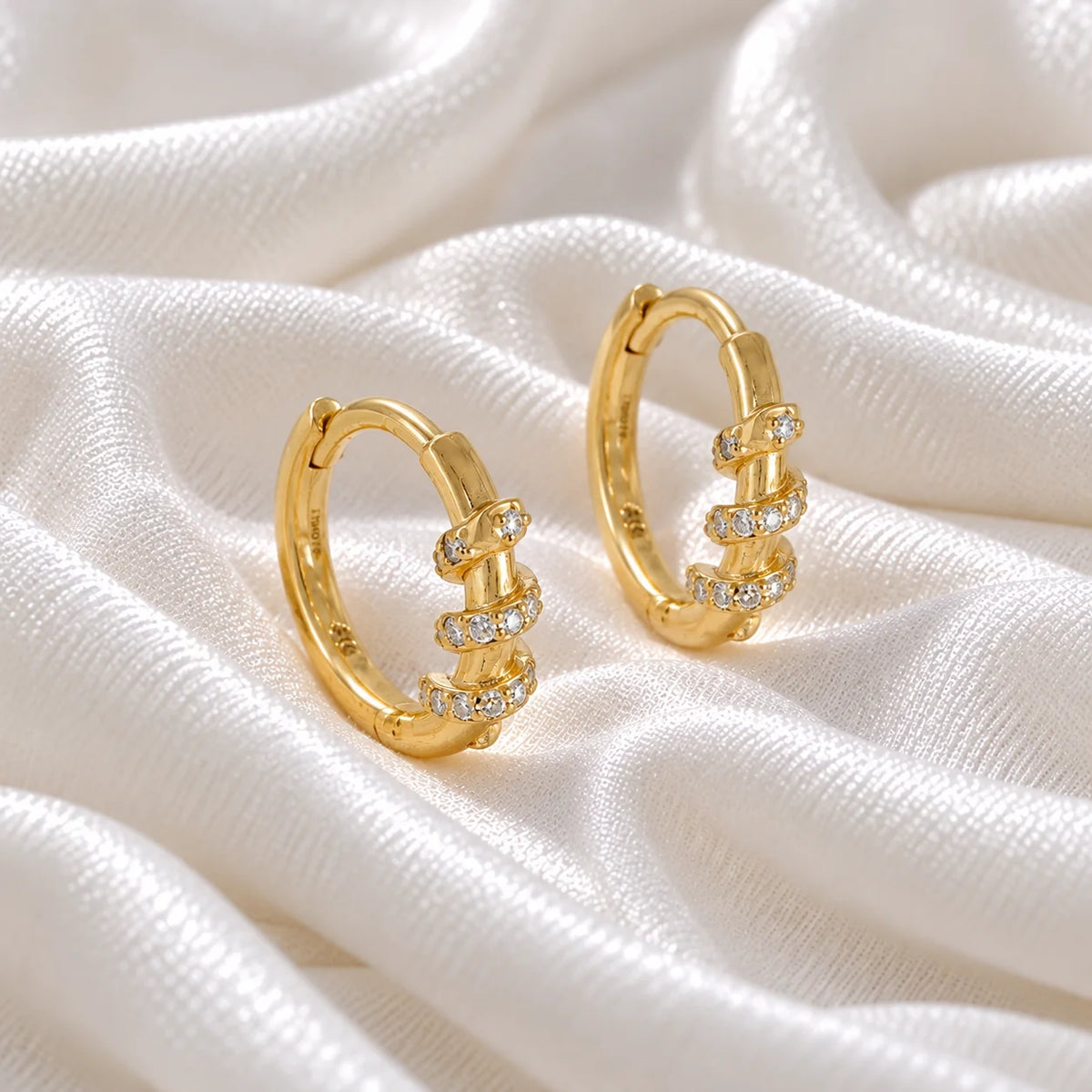 Diamond_hoop_earrings_in_gold_plated_silver_with_a_twisted_design_band_at_front_angle_view_on_soft_fabric_background
