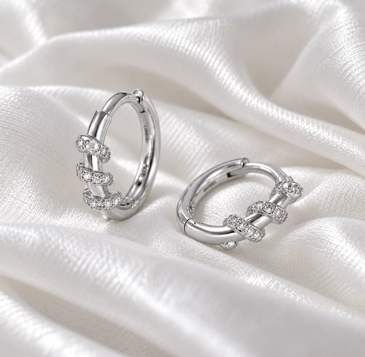 Diamond_hoop_earrings_in_sterling_silver_with_a_twisted_design_band_at_side_angle_view_on_soft_fabric_background