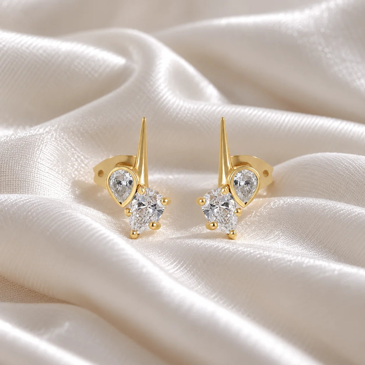 Diamond_stud_earrings_in_gold_plated_silver_with_teardrop_shaped_diamonds_at_front_angle_view_on_soft_fabric_background