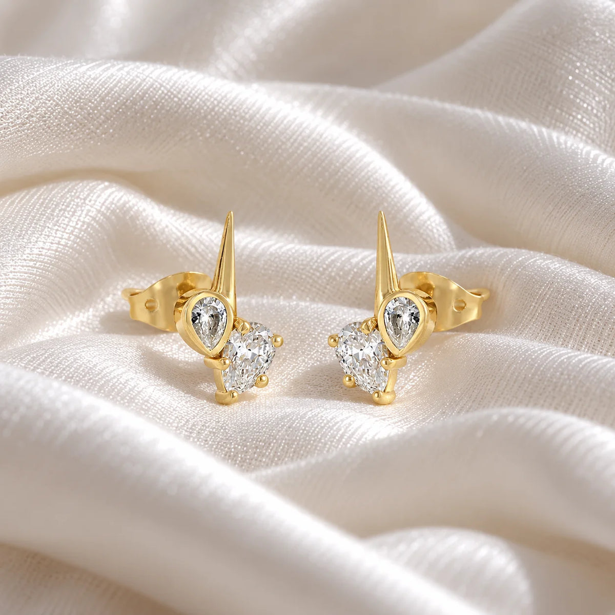 Diamond_stud_earrings_in_gold_plated_silver_with_teardrop_shaped_diamonds_at_slight_angle_view_on_soft_fabric_background