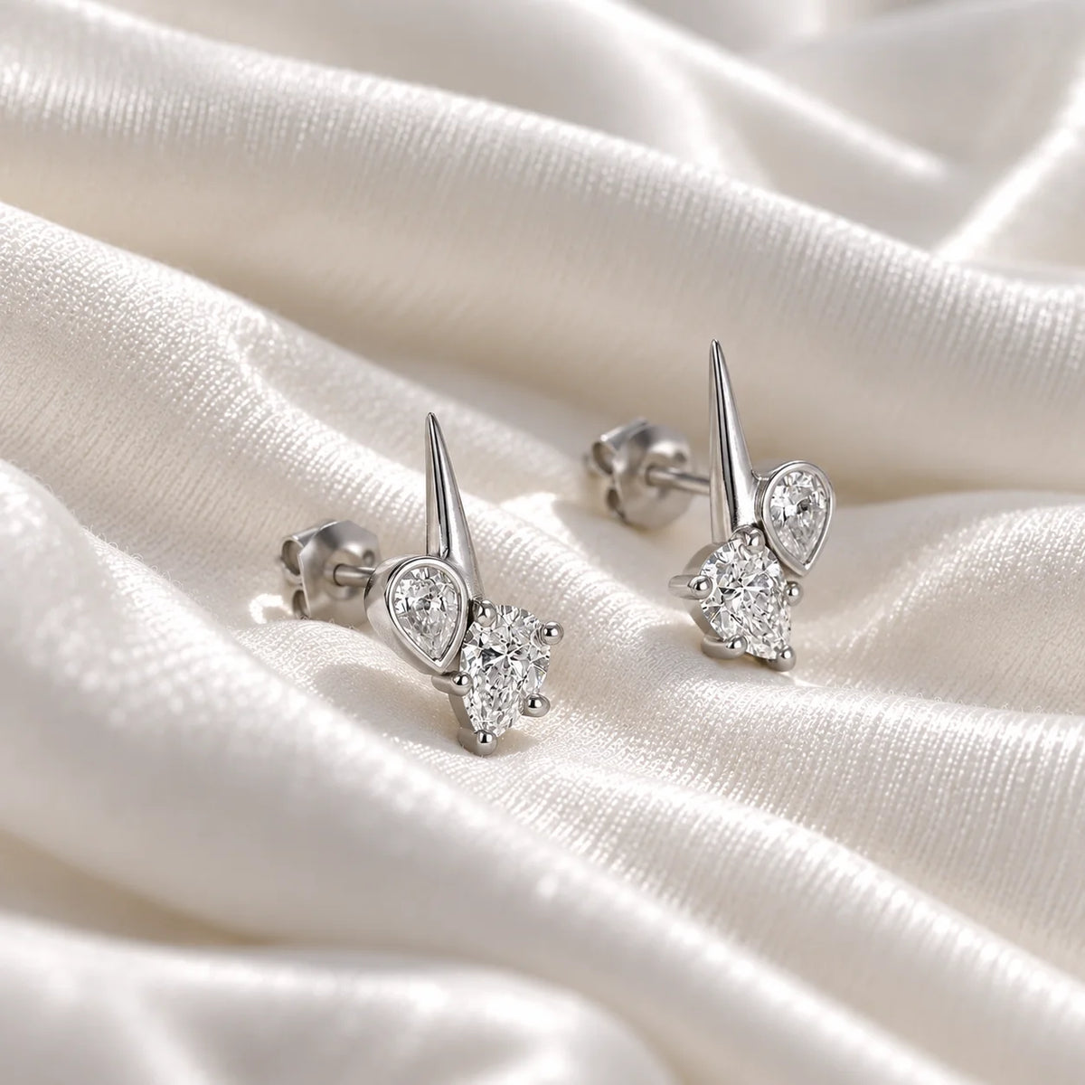 Diamond_stud_earrings_in_sterling_silver_with_teardrop_shaped_diamonds_at_slight_angle_view_on_soft_fabric_background