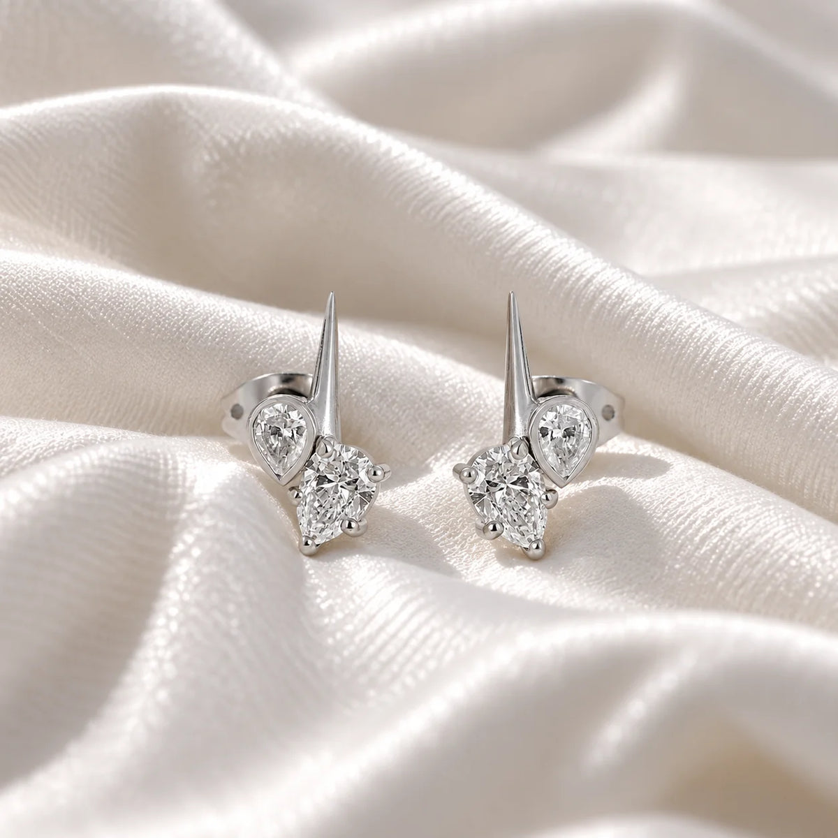Diamond_stud_earrings_in_sterling_silver_with_teardrop_shaped_diamonds_at_front_angle_view_on_soft_fabric_background
