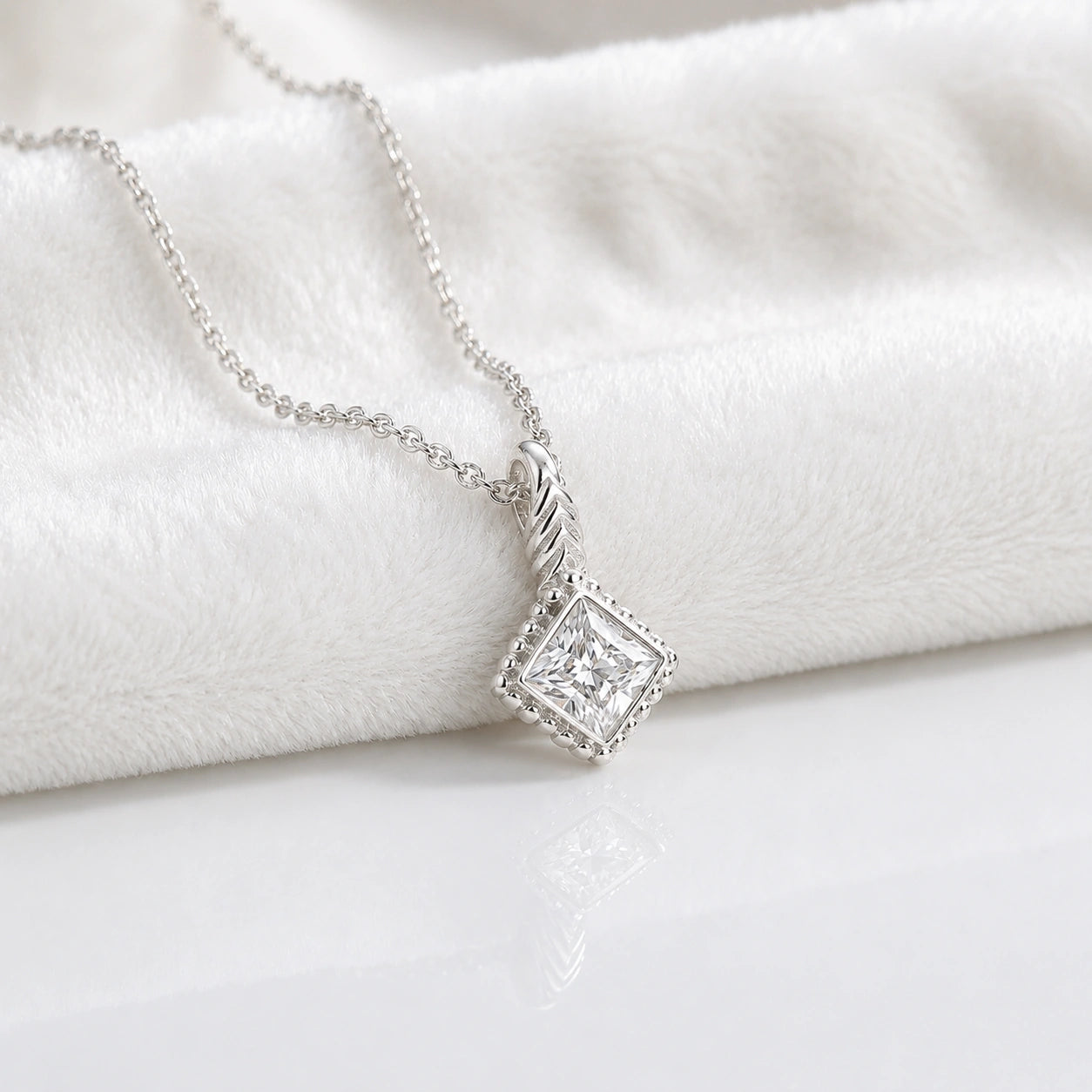 Birthstone_necklace_in_sterling_silver_with_square_cut_diamond_pendant_in_slighlty_angled_view_on_soft_white_fabric_background