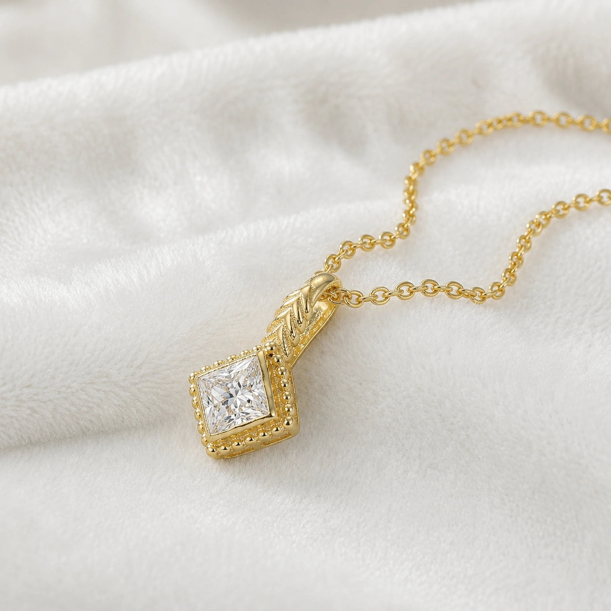 Birthstone_necklace_in_gold_plated_silver_with_square_cut_diamond_pendant_in_slighlty_angled_view_on_soft_white_fabric_background