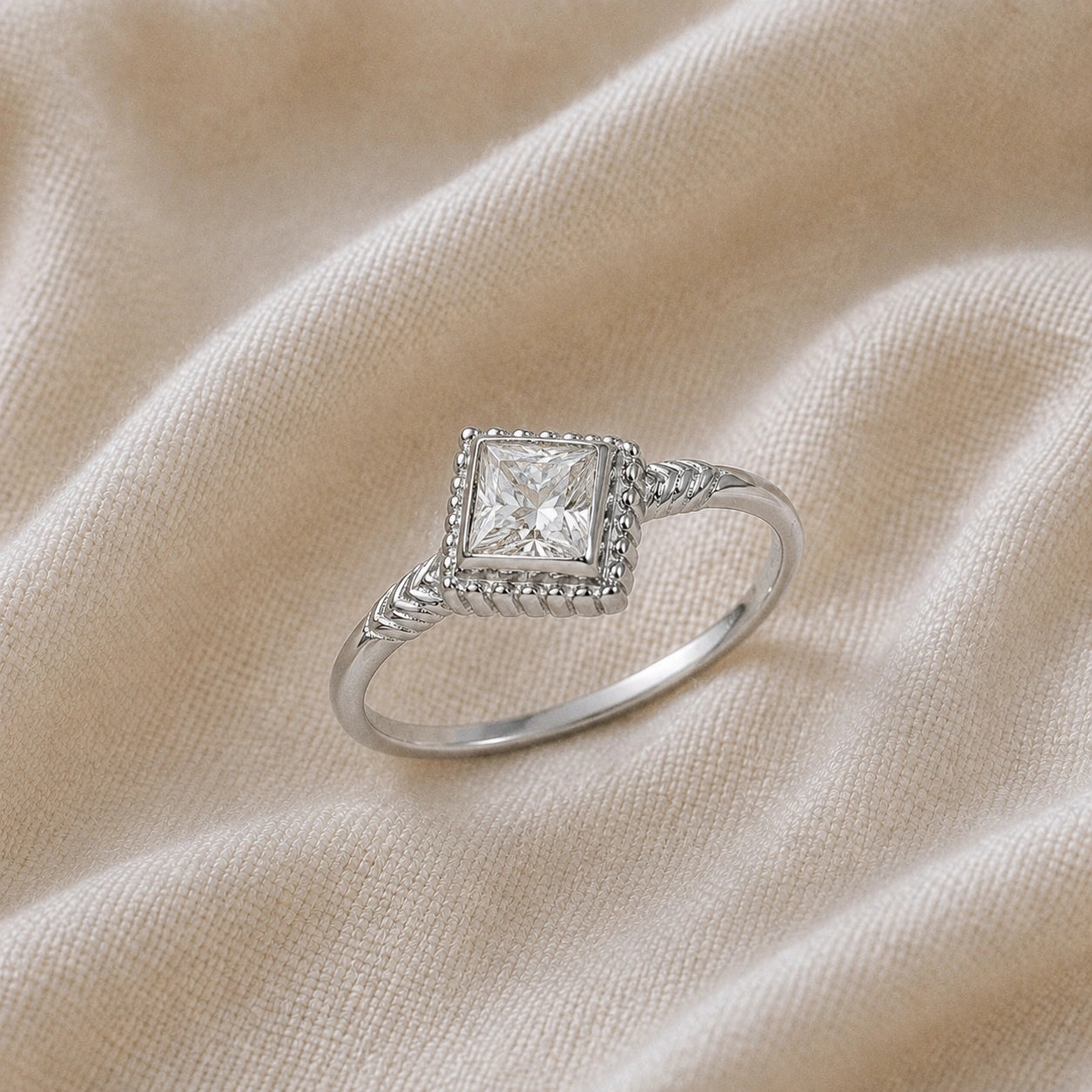 Princess_cut_ring_sterling_silver_with_square_diamond_and_detailed_band_slightly_tilted_view_on_soft_fabric_background