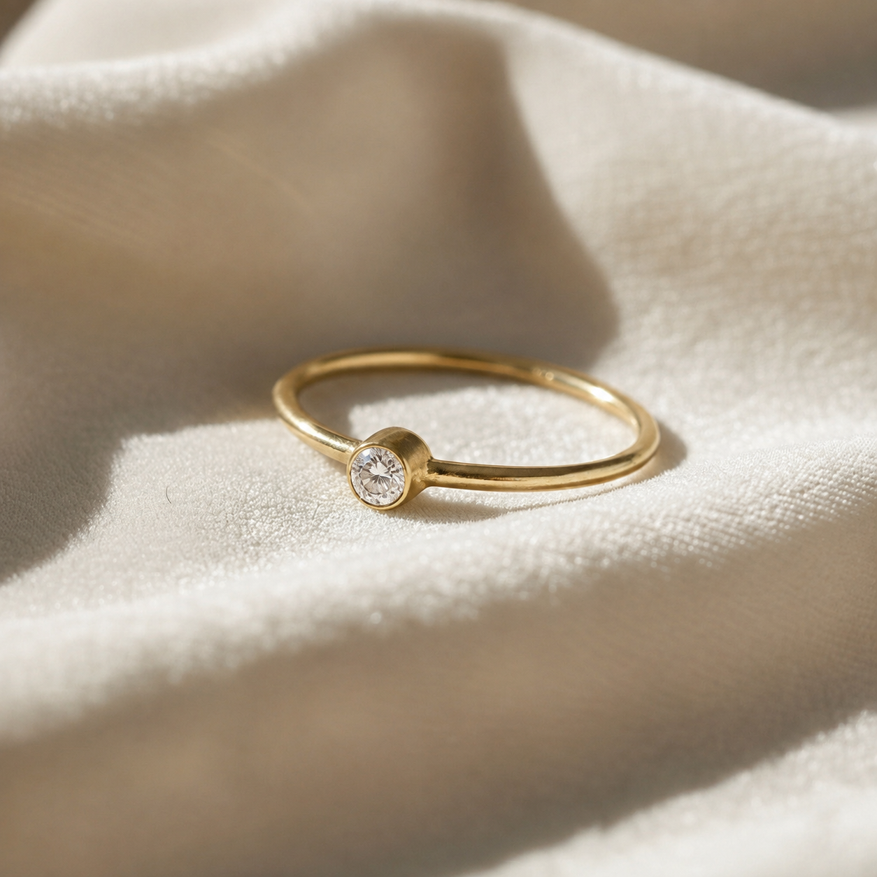 A gold plated birthstone ring featuring a diamond gemstone, styled as a delicate stacking ring on a soft white fabric background