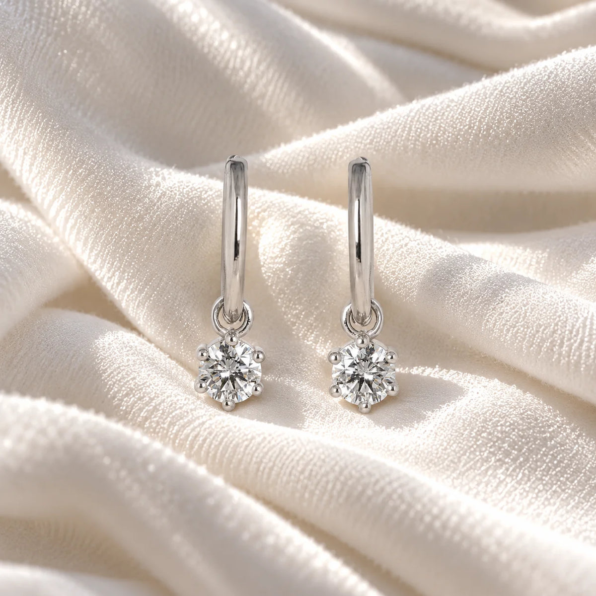 Diamond_earrings_in_sterling_silver_with_a_hoop_drop_design_at_front_angle_view_on_soft_fabric_background