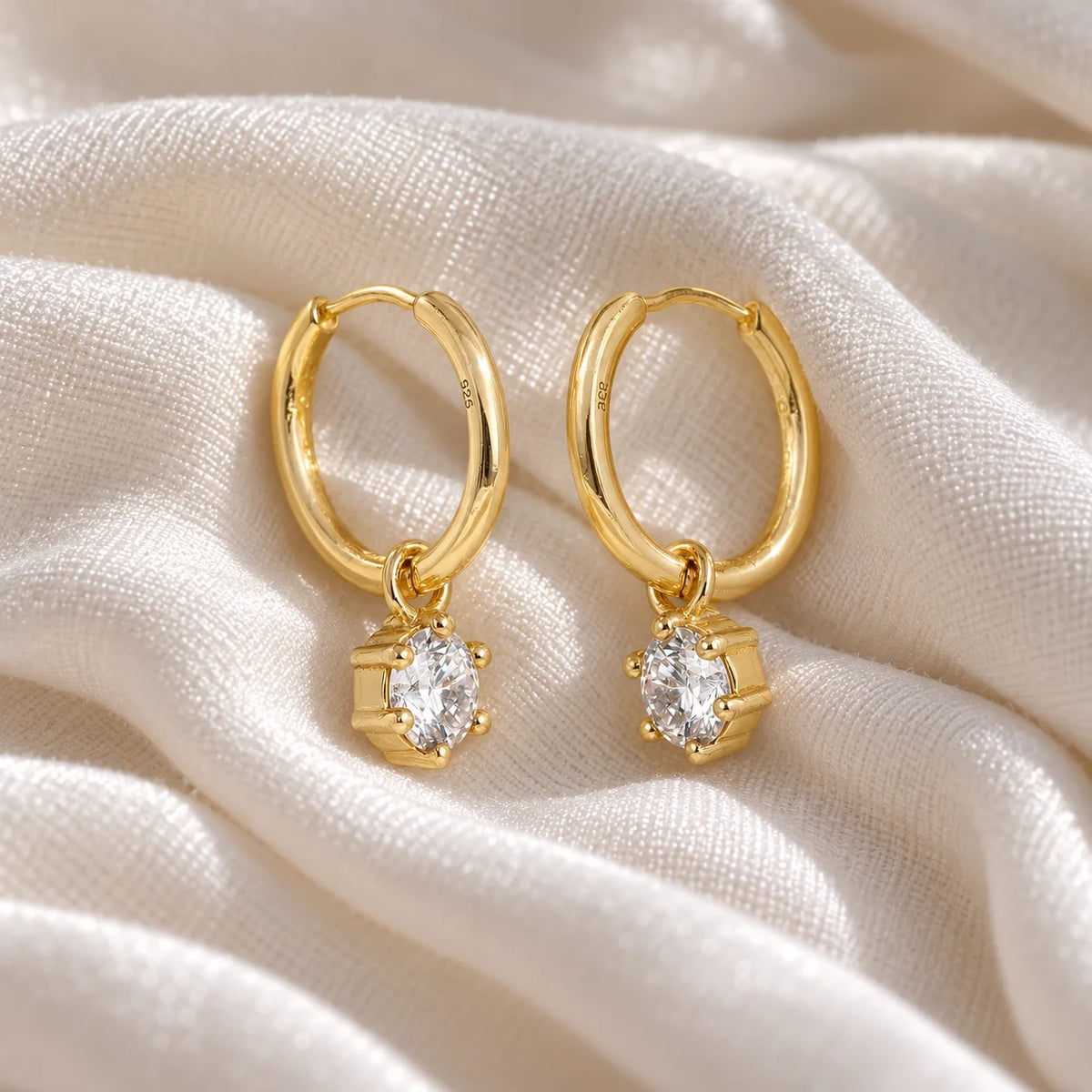 Diamond_earrings_in_gold_plated_silver_with_a_hoop_drop_design_at_slight_angled_view_on_soft_fabric_background