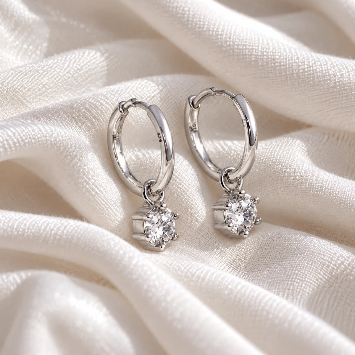 Diamond_earrings_in_sterling_silver_with_a_hoop_drop_design_at_slight_angled_view_on_soft_fabric_background