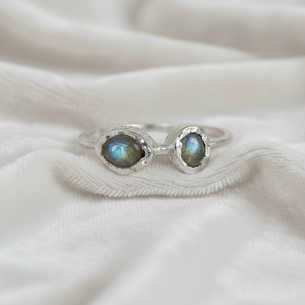 Double stone ring featuring two oval labradorite gems in rugged silver settings on a white cloth straight-on angle