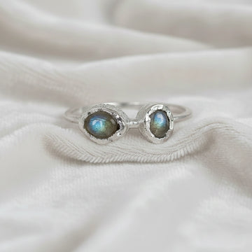 Double stone ring featuring two oval labradorite gems in rugged silver settings on a white cloth straight-on angle